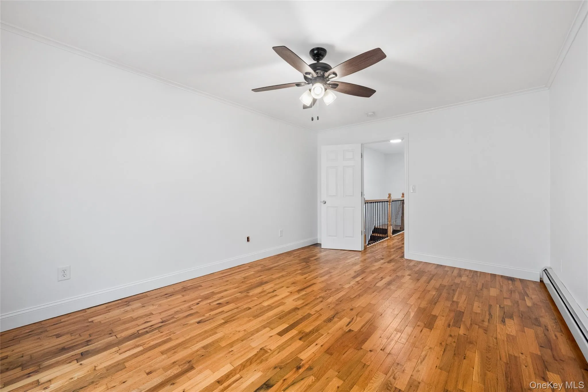 Empty room with light wood-style flooring, a baseboard radiator, crown molding, and a ceiling fan Empty room with light wood-style flooring, a baseboard radiator, crown molding, and a ceiling fan