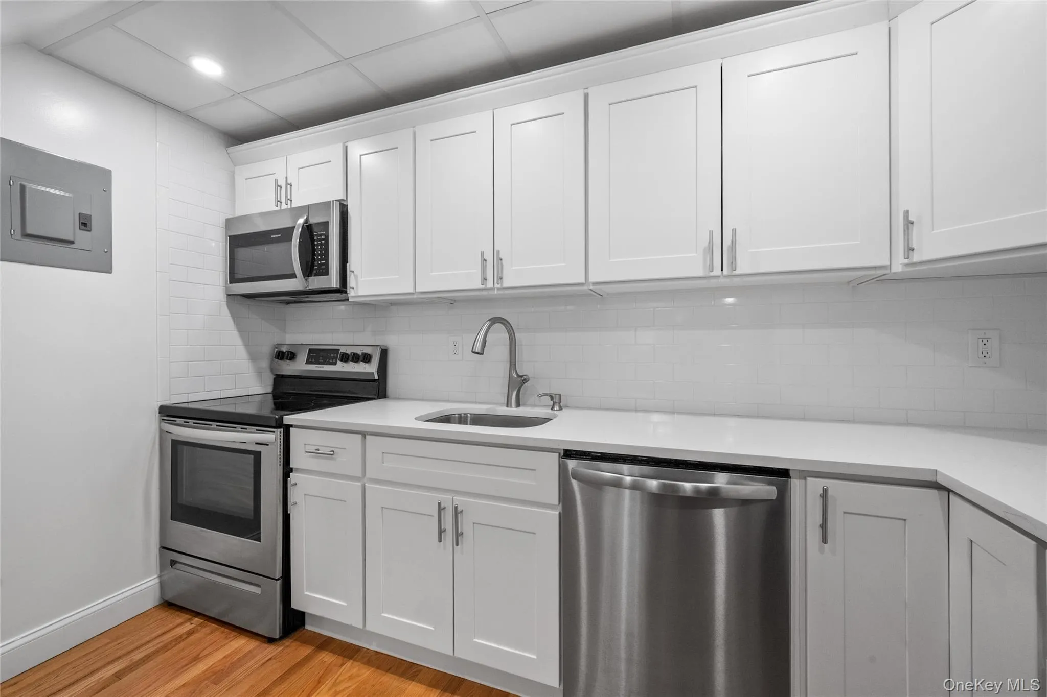 Kitchen with stainless steel appliances, decorative backsplash, white cabinets, light wood-style flooring, and electric panel Kitchen with stainless steel appliances, decorative backsplash, white cabinets, light wood-style flooring, and electric panel