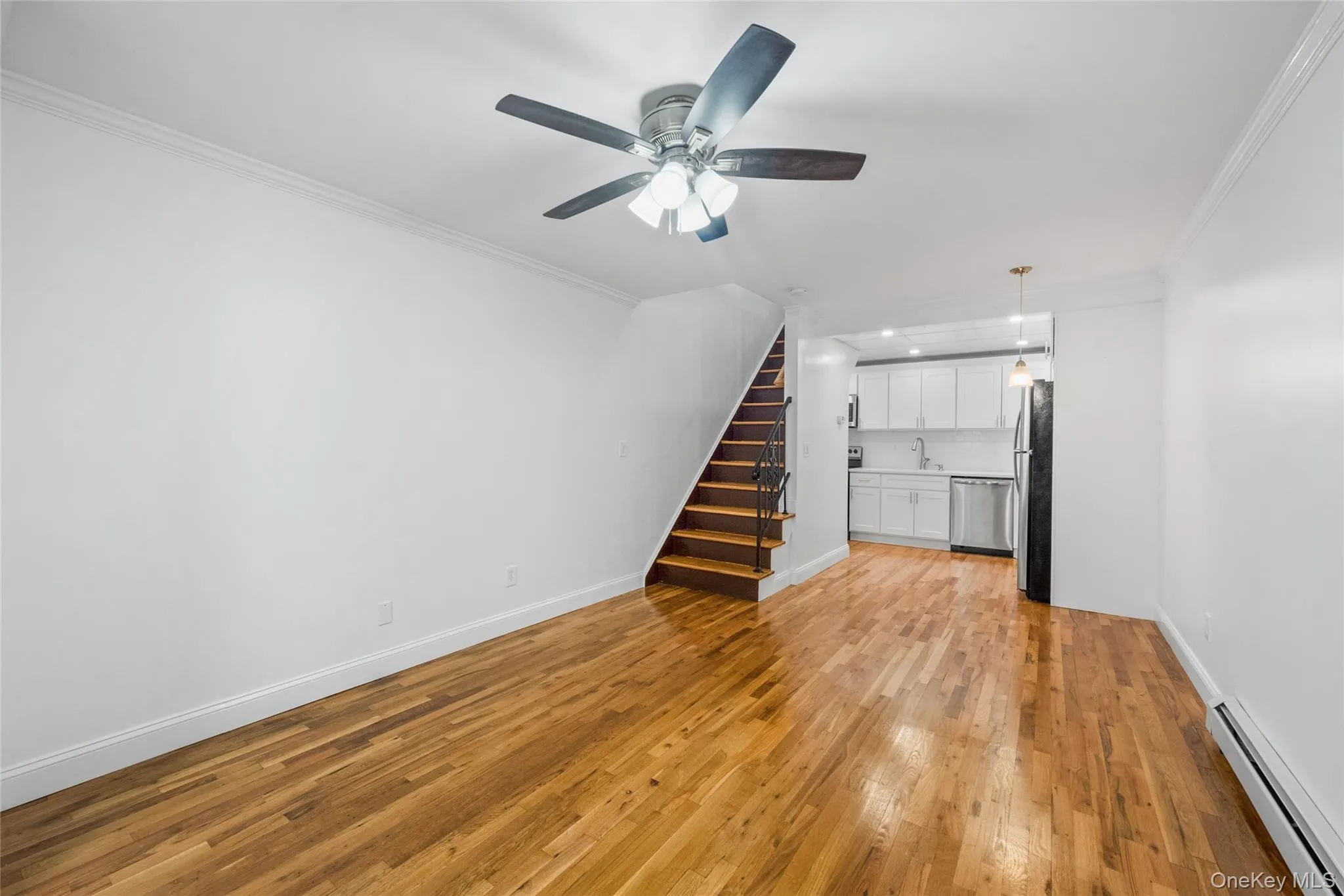 Unfurnished living room featuring crown molding, a baseboard heating unit, stairway, light wood-style floors, and ceiling fan Unfurnished living room featuring crown molding, a baseboard heating unit, stairway, light wood-style floors, and ceiling fan