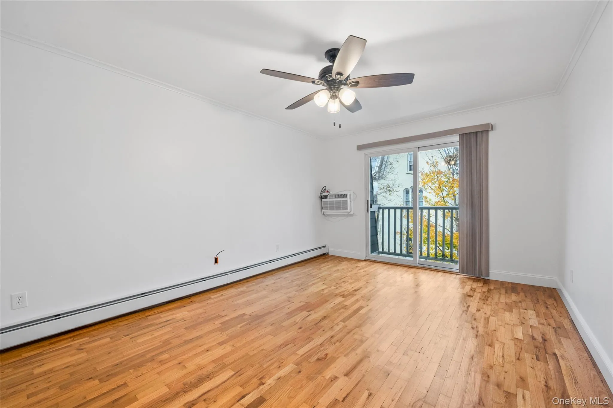 Spare room with a baseboard radiator, light wood-type flooring, crown molding, a ceiling fan, and an AC wall unit Spare room with a baseboard radiator, light wood-type flooring, crown molding, a ceiling fan, and an AC wall unit