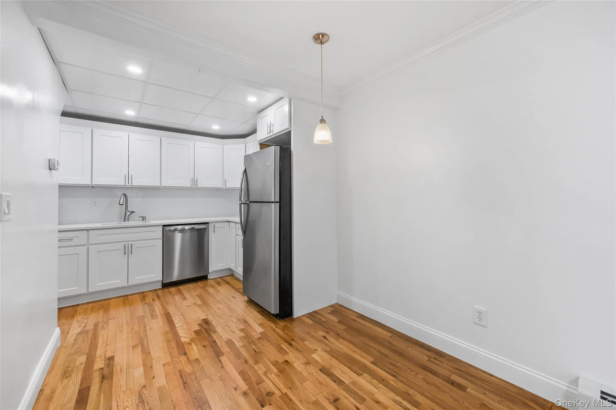Kitchen featuring white cabinetry, light countertops, appliances with stainless steel finishes, light wood-style floors, and a baseboard radiator Kitchen featuring white cabinetry, light countertops, appliances with stainless steel finishes, light wood-style floors, and a baseboard radiator
