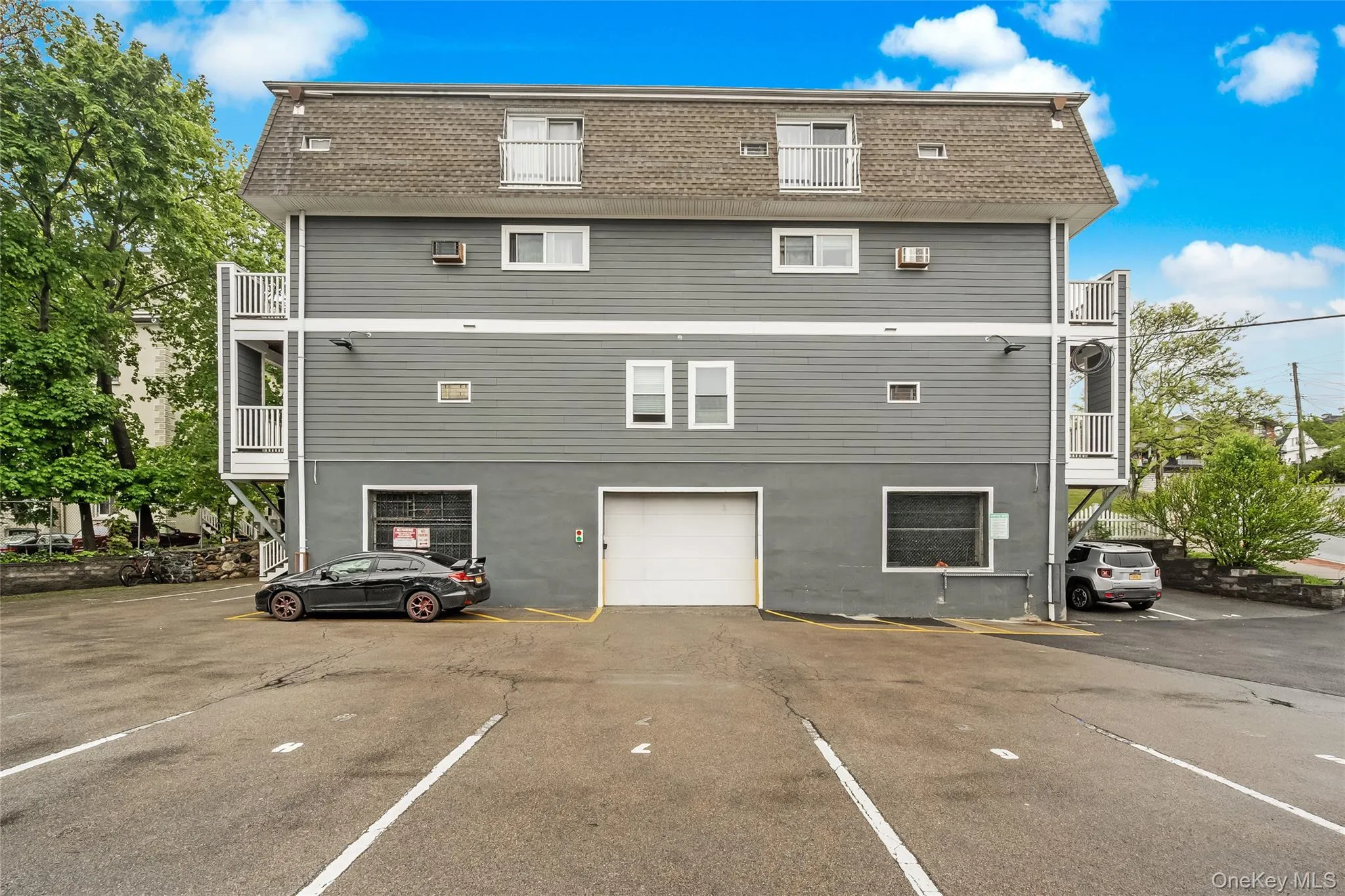 Rear view of house featuring mansard roof, roof with shingles, and uncovered parking Rear view of house featuring mansard roof, roof with shingles, and uncovered parking