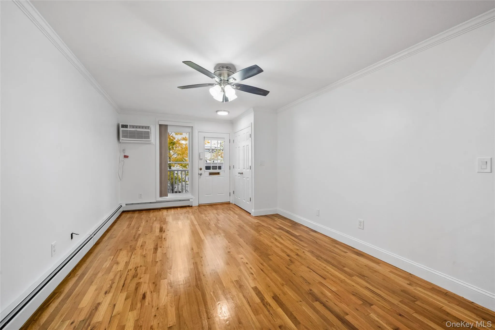 Empty room featuring a baseboard heating unit, light wood-type flooring, crown molding, a ceiling fan, and a wall mounted air conditioner Empty room featuring a baseboard heating unit, light wood-type flooring, crown molding, a ceiling fan, and a wall mounted air conditioner