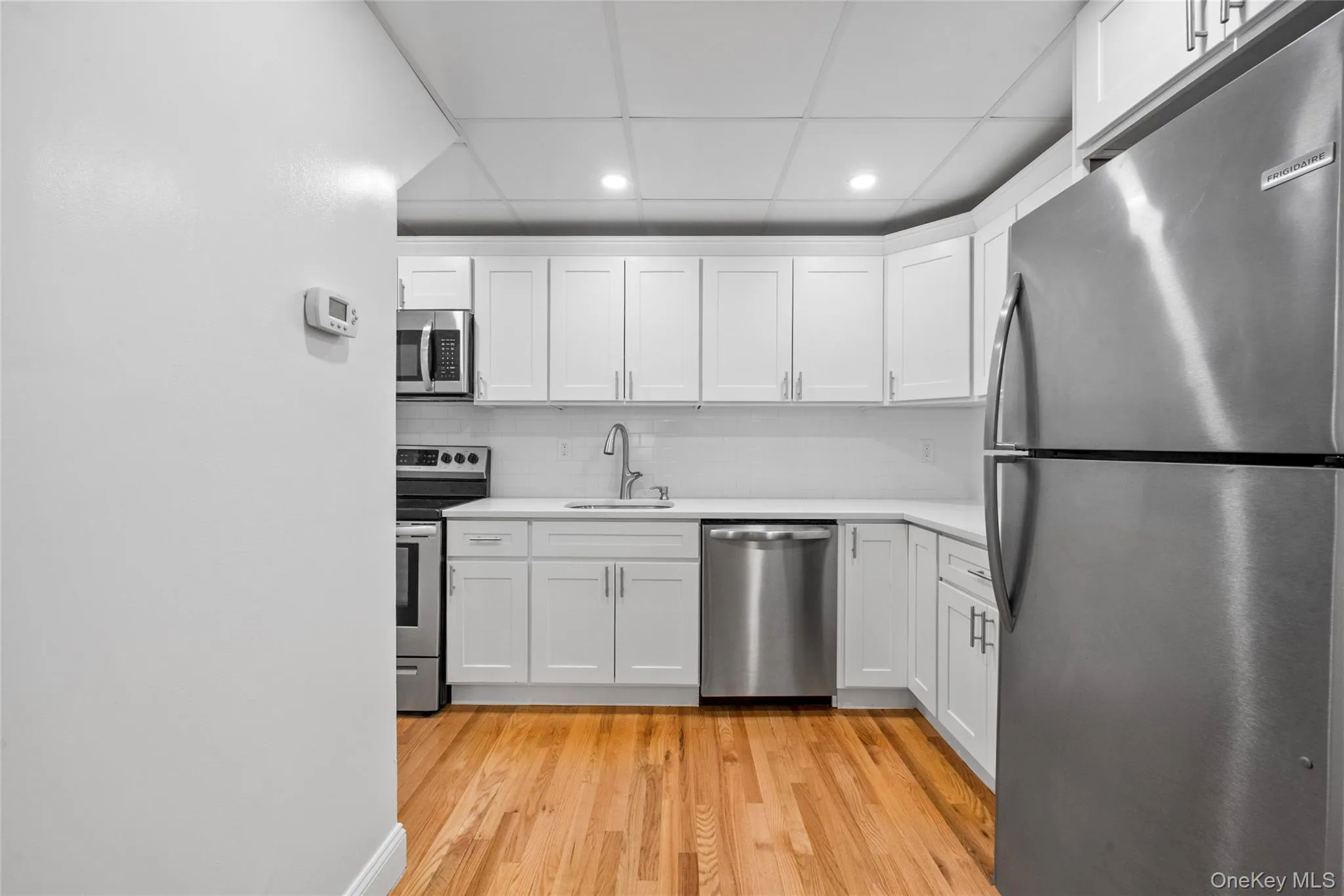 Kitchen with appliances with stainless steel finishes, white cabinetry, light wood-type flooring, recessed lighting, and tasteful backsplash Kitchen with appliances with stainless steel finishes, white cabinetry, light wood-type flooring, recessed lighting, and tasteful backsplash