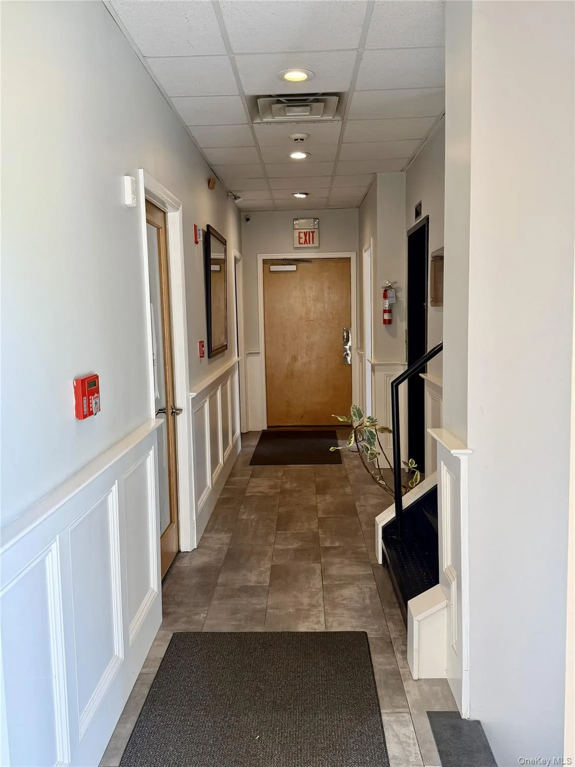 Hallway featuring a paneled ceiling, a decorative wall, and wainscoting Hallway featuring a paneled ceiling, a decorative wall, and wainscoting