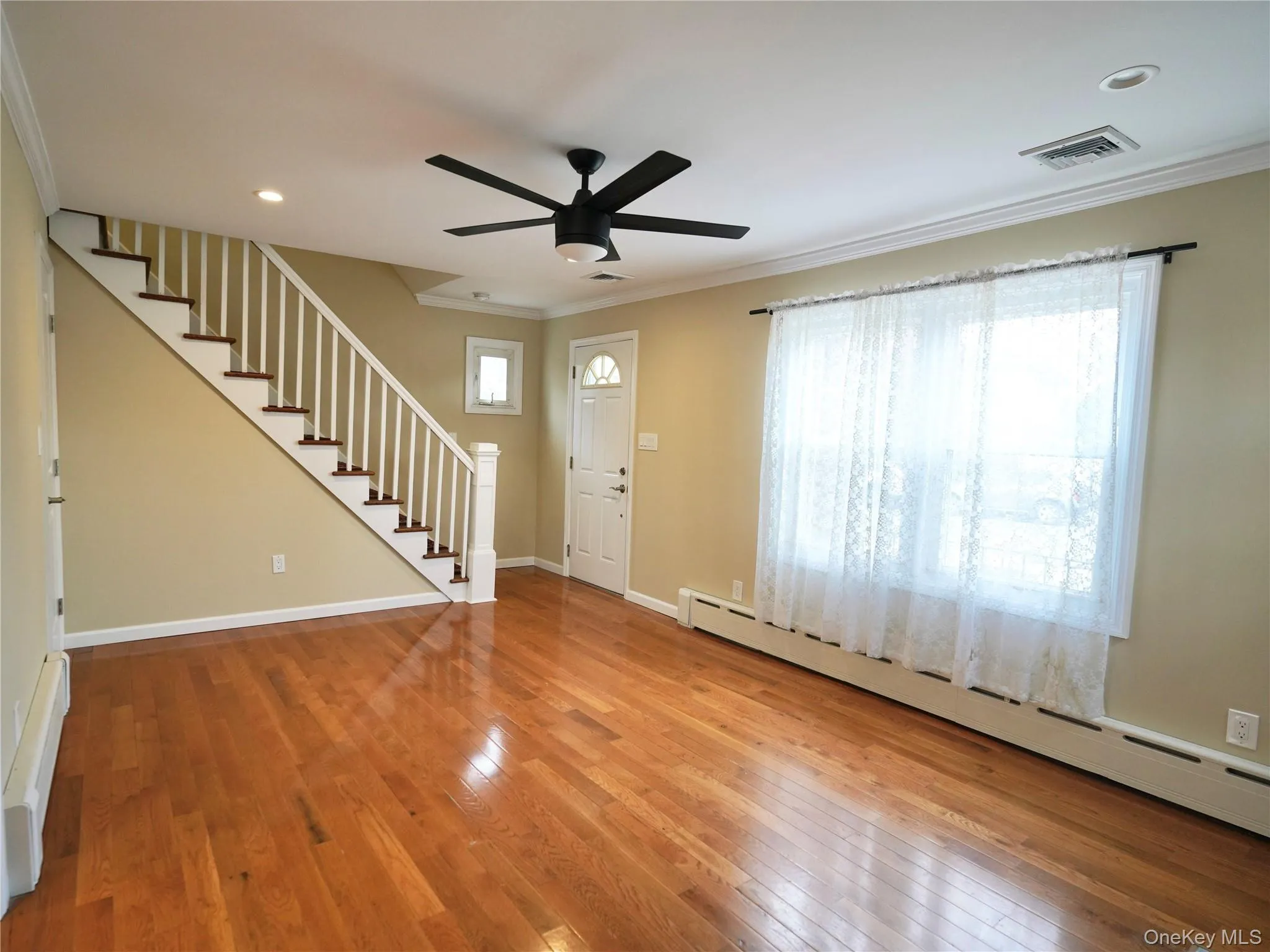 Foyer entrance featuring a baseboard heating unit, stairway, ornamental molding, light wood finished floors, and ceiling fan Foyer entrance featuring a baseboard heating unit, stairway, ornamental molding, light wood finished floors, and ceiling fan
