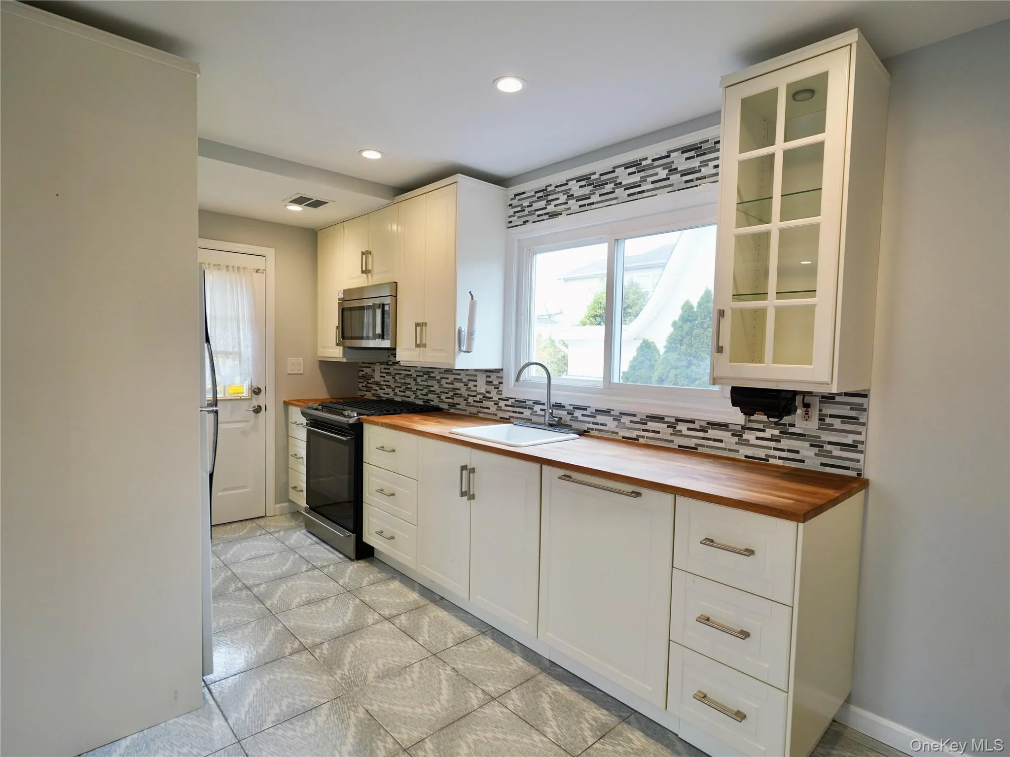 Kitchen with wood counters, glass insert cabinets, black gas range, stainless steel microwave, and recessed lighting Kitchen with wood counters, glass insert cabinets, black gas range, stainless steel microwave, and recessed lighting