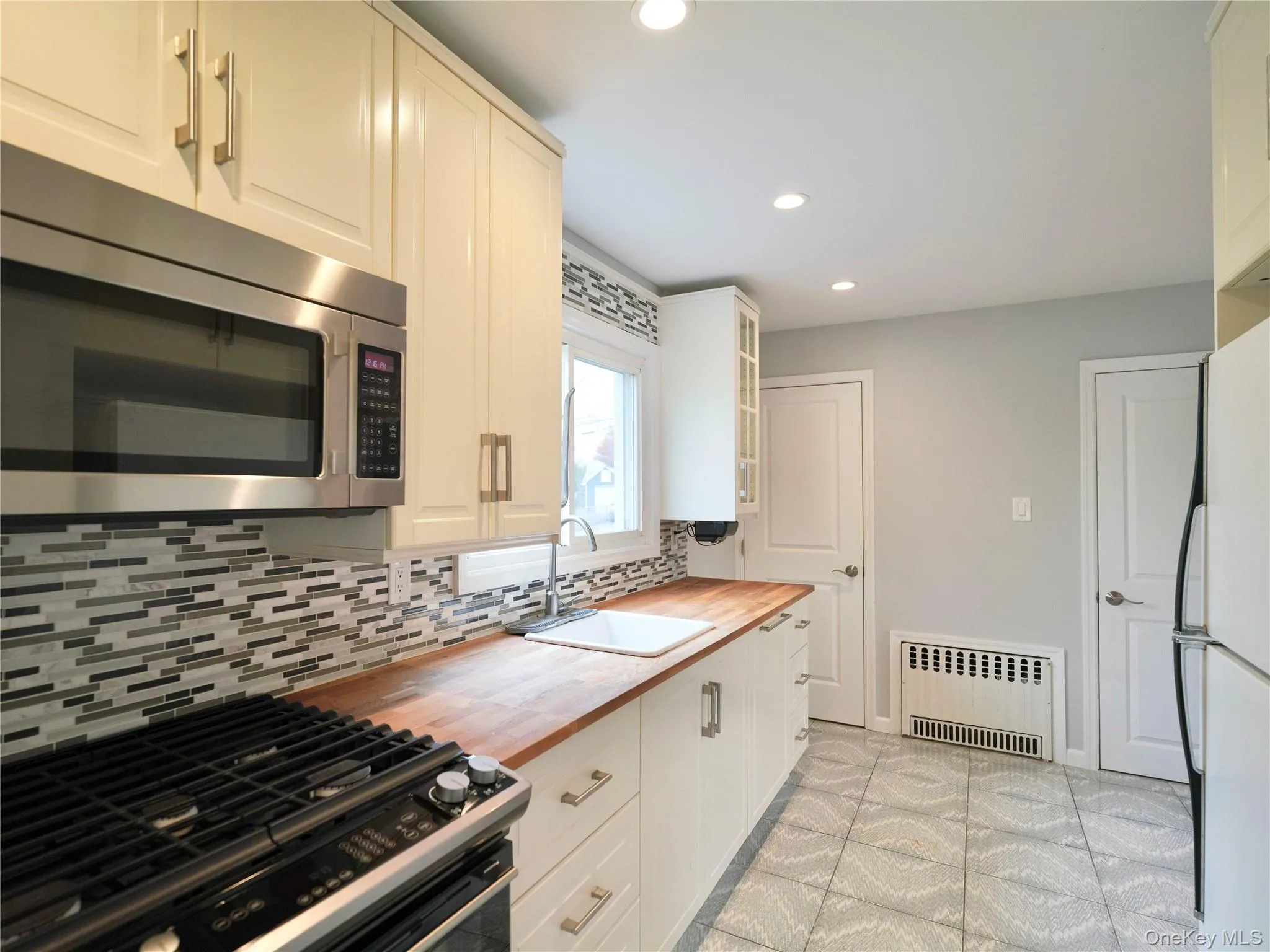 Kitchen with wooden counters, stainless steel appliances, radiator heating unit, recessed lighting, and glass insert cabinets Kitchen with wooden counters, stainless steel appliances, radiator heating unit, recessed lighting, and glass insert cabinets