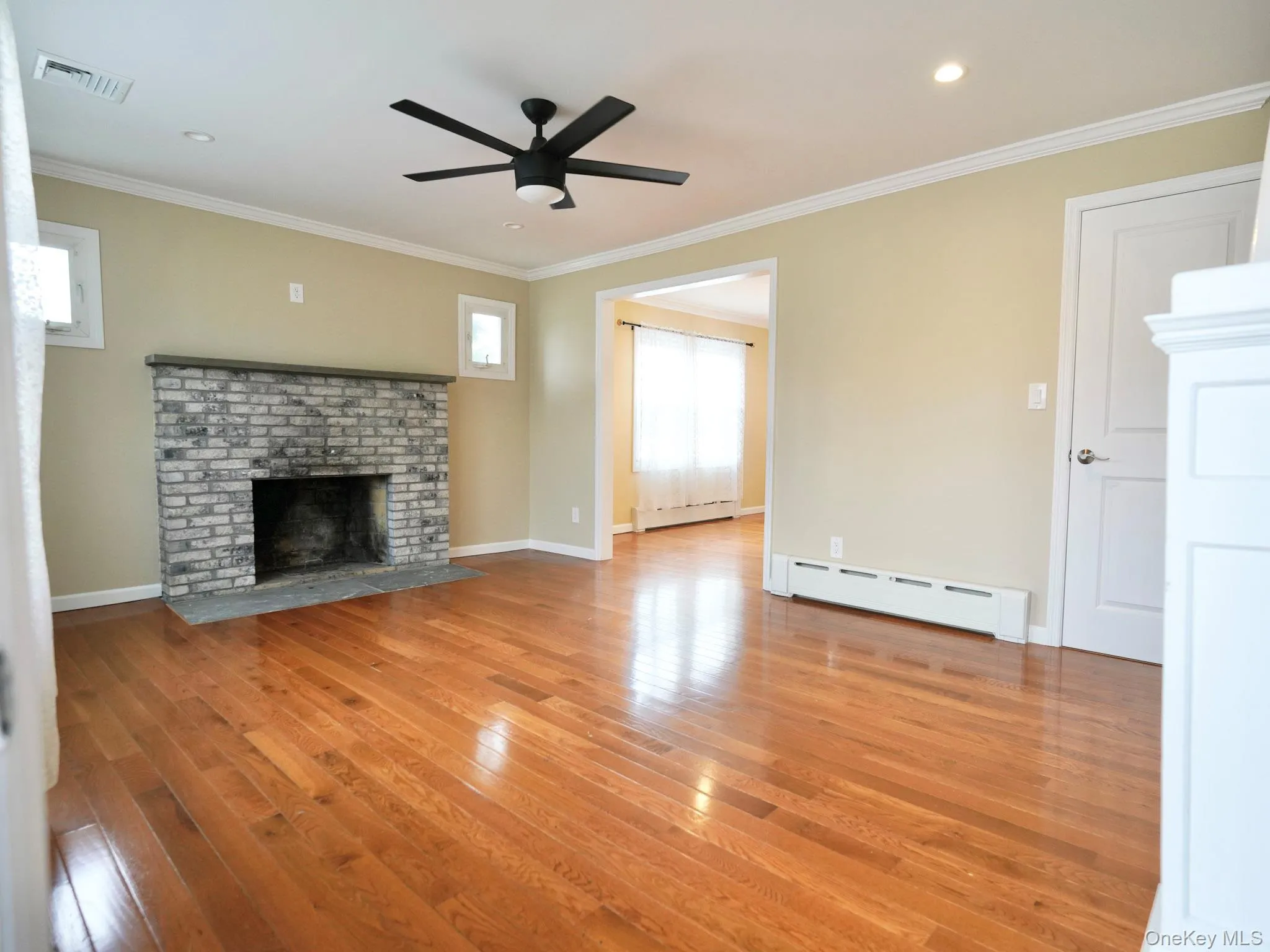 Unfurnished living room featuring a baseboard radiator, a fireplace, crown molding, a ceiling fan, and light wood-style flooring Unfurnished living room featuring a baseboard radiator, a fireplace, crown molding, a ceiling fan, and light wood-style flooring