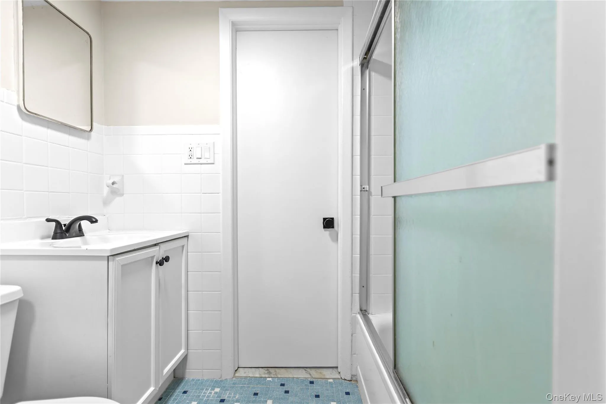 Full bath with tile walls, vanity, enclosed tub / shower combo, wainscoting, and light tile patterned floors Full bath with tile walls, vanity, enclosed tub / shower combo, wainscoting, and light tile patterned floors