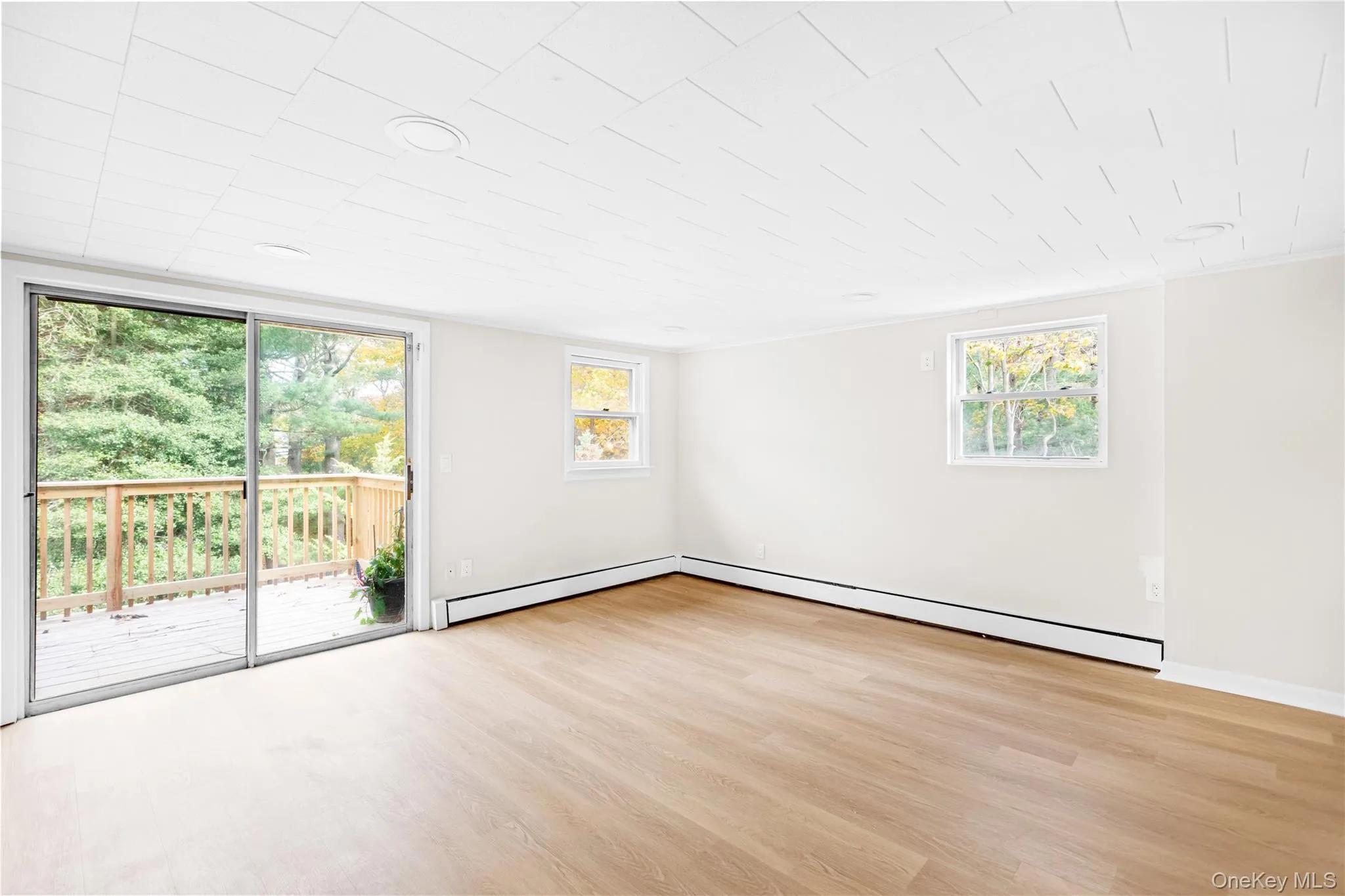 Unfurnished room with light wood-style flooring, healthy amount of natural light, and baseboard heating Unfurnished room with light wood-style flooring, healthy amount of natural light, and baseboard heating