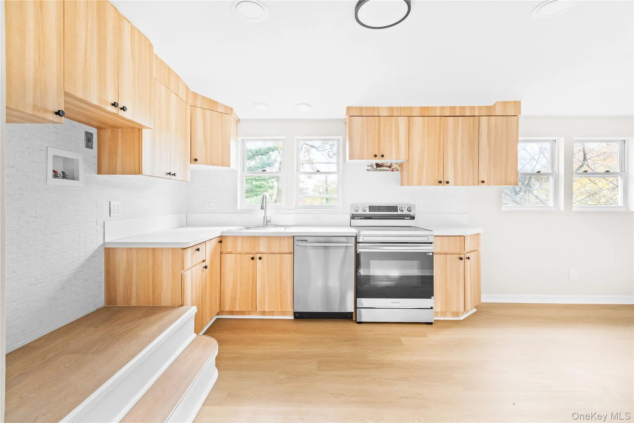 Kitchen with light brown cabinetry, appliances with stainless steel finishes, light wood-style flooring, light countertops, and recessed lighting Kitchen with light brown cabinetry, appliances with stainless steel finishes, light wood-style flooring, light countertops, and recessed lighting