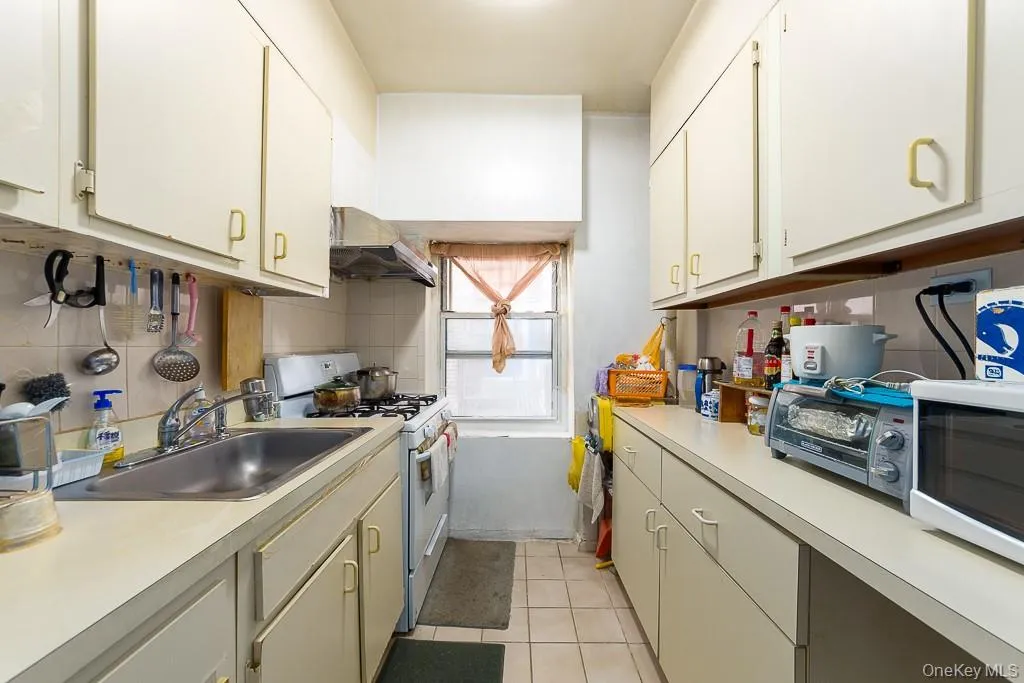 Kitchen with white appliances, light tile patterned flooring, under cabinet range hood, and light countertops Kitchen with white appliances, light tile patterned flooring, under cabinet range hood, and light countertops