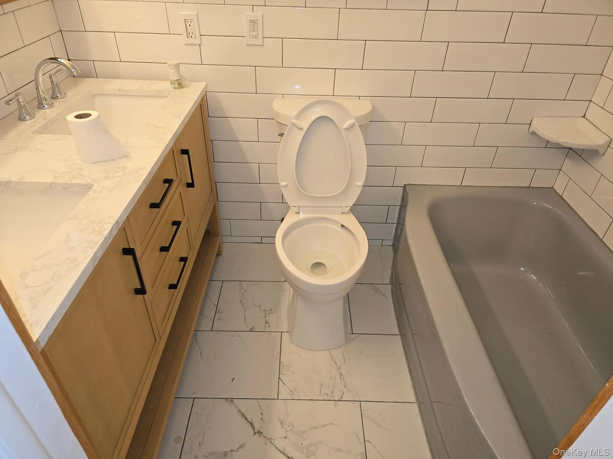 Bathroom with double vanity, a bath, tile walls, and light marble finish flooring Bathroom with double vanity, a bath, tile walls, and light marble finish flooring