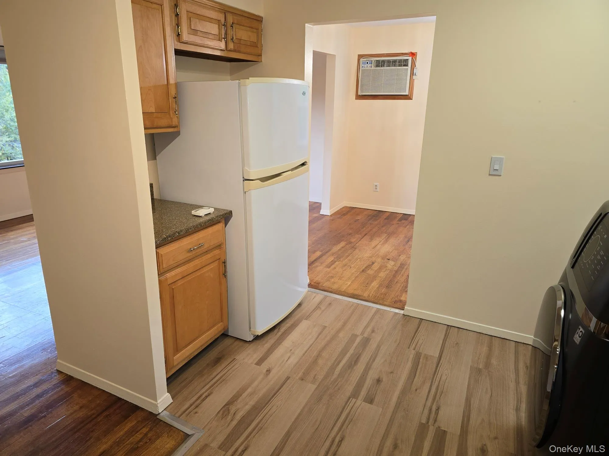 Kitchen featuring light wood-type flooring, freestanding refrigerator, washer / clothes dryer, brown cabinets, and a wall unit AC Kitchen featuring light wood-type flooring, freestanding refrigerator, washer / clothes dryer, brown cabinets, and a wall unit AC