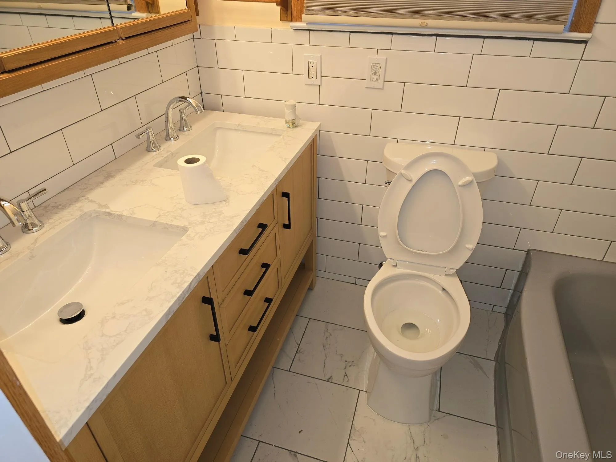 Bathroom with double vanity, a bathtub, tile walls, light marble finish floors, and decorative backsplash Bathroom with double vanity, a bathtub, tile walls, light marble finish floors, and decorative backsplash