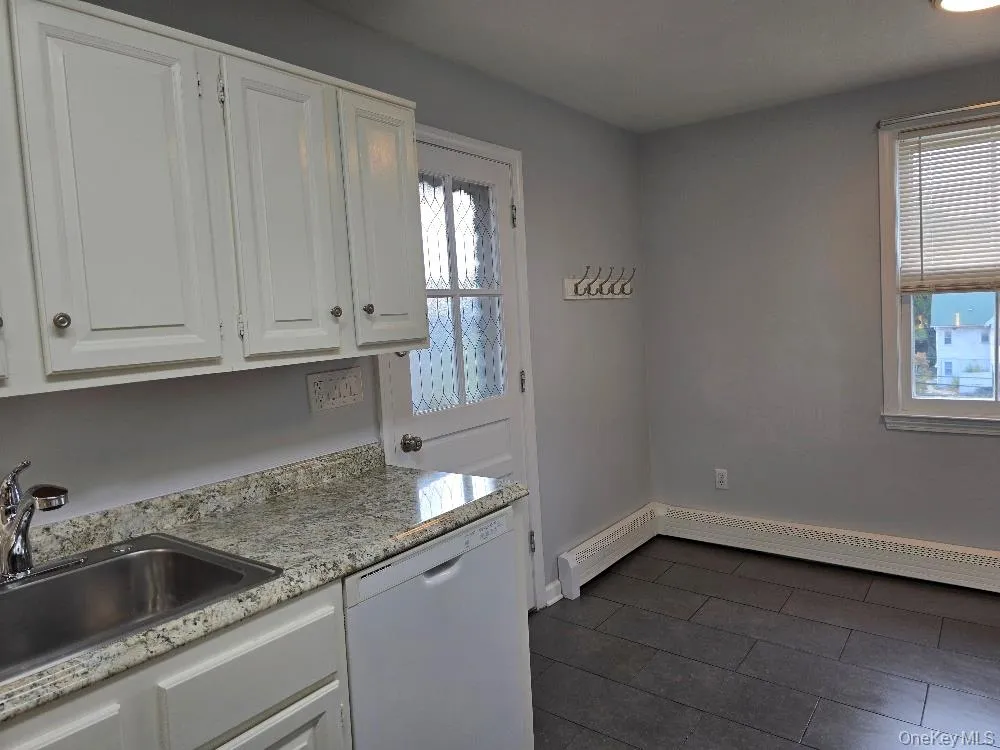 Kitchen featuring white cabinets, white dishwasher, baseboard heating, and light stone countertops Kitchen featuring white cabinets, white dishwasher, baseboard heating, and light stone countertops