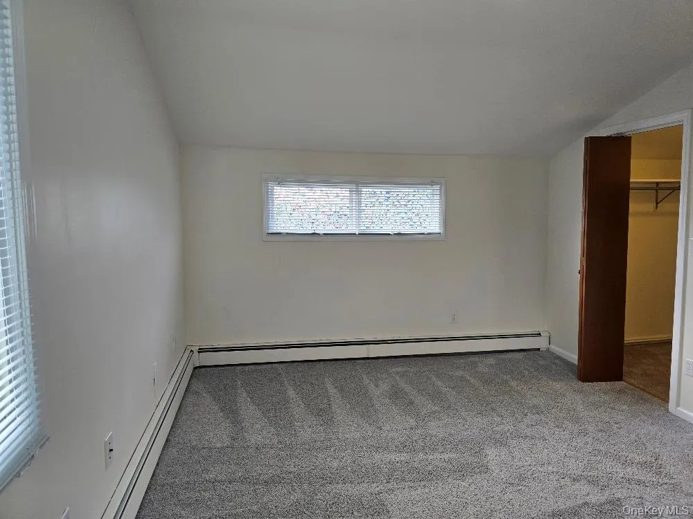 Unfurnished bedroom featuring lofted ceiling, a baseboard heating unit, a walk in closet, and carpet Unfurnished bedroom featuring lofted ceiling, a baseboard heating unit, a walk in closet, and carpet