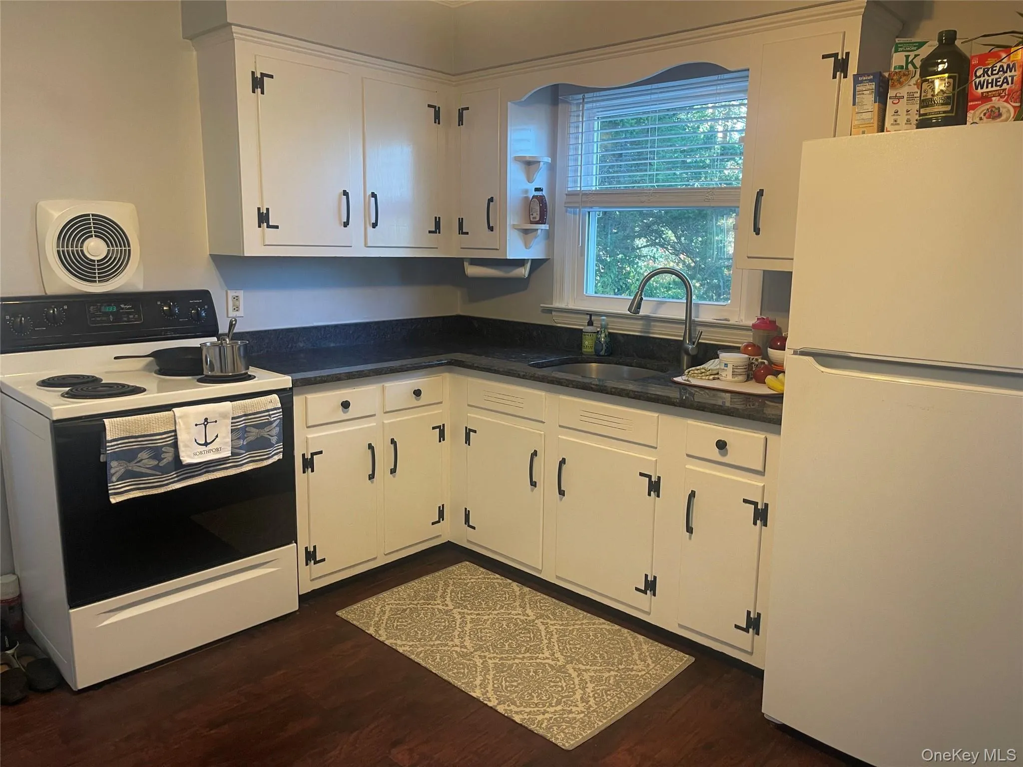 Kitchen featuring white appliances, white cabinetry, dark wood-style floors, and dark stone counters Kitchen featuring white appliances, white cabinetry, dark wood-style floors, and dark stone counters