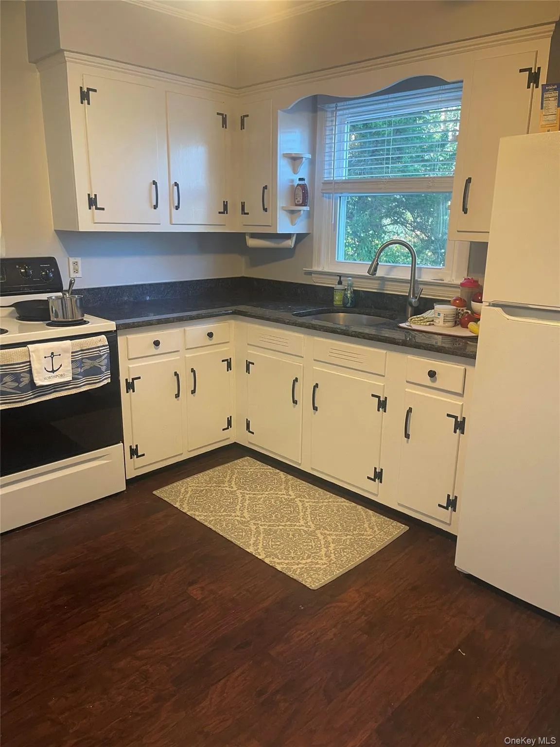 Kitchen featuring white appliances, white cabinets, dark wood-type flooring, and dark stone counters Kitchen featuring white appliances, white cabinets, dark wood-type flooring, and dark stone counters