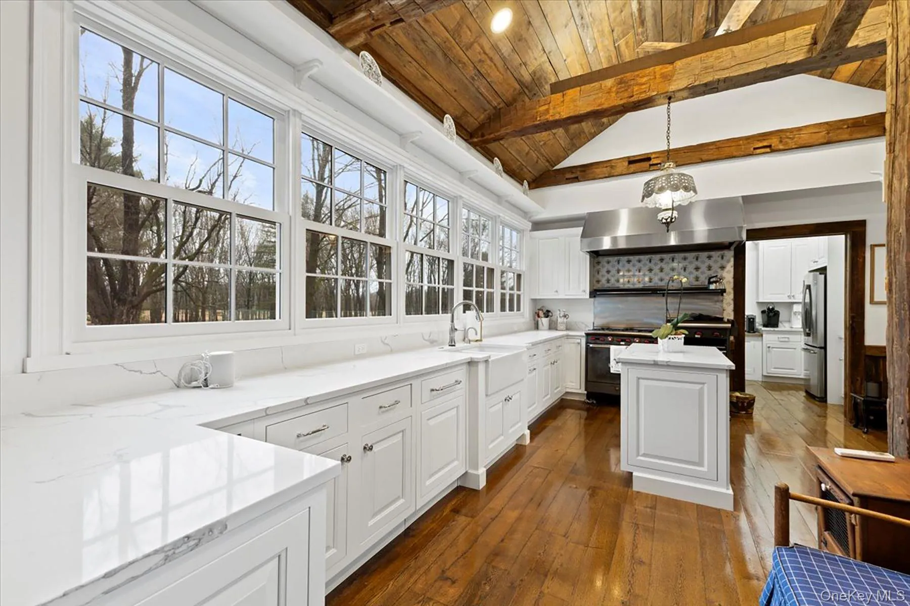 Kitchen with backsplash, white cabinetry, range hood, hanging light fixtures, and wood ceiling Kitchen with backsplash, white cabinetry, range hood, hanging light fixtures, and wood ceiling