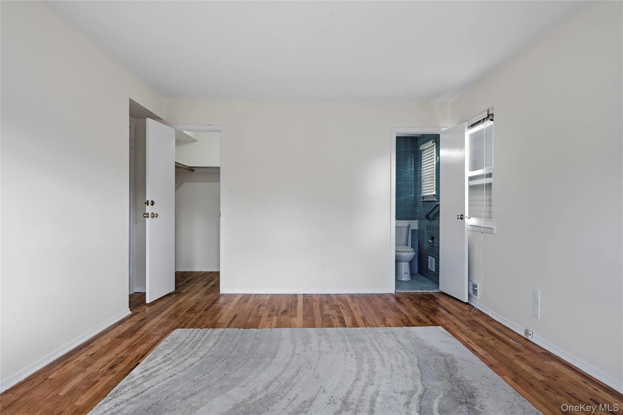 Unfurnished bedroom featuring wood finished floors, ensuite bath, and a walk in closet Unfurnished bedroom featuring wood finished floors, ensuite bath, and a walk in closet