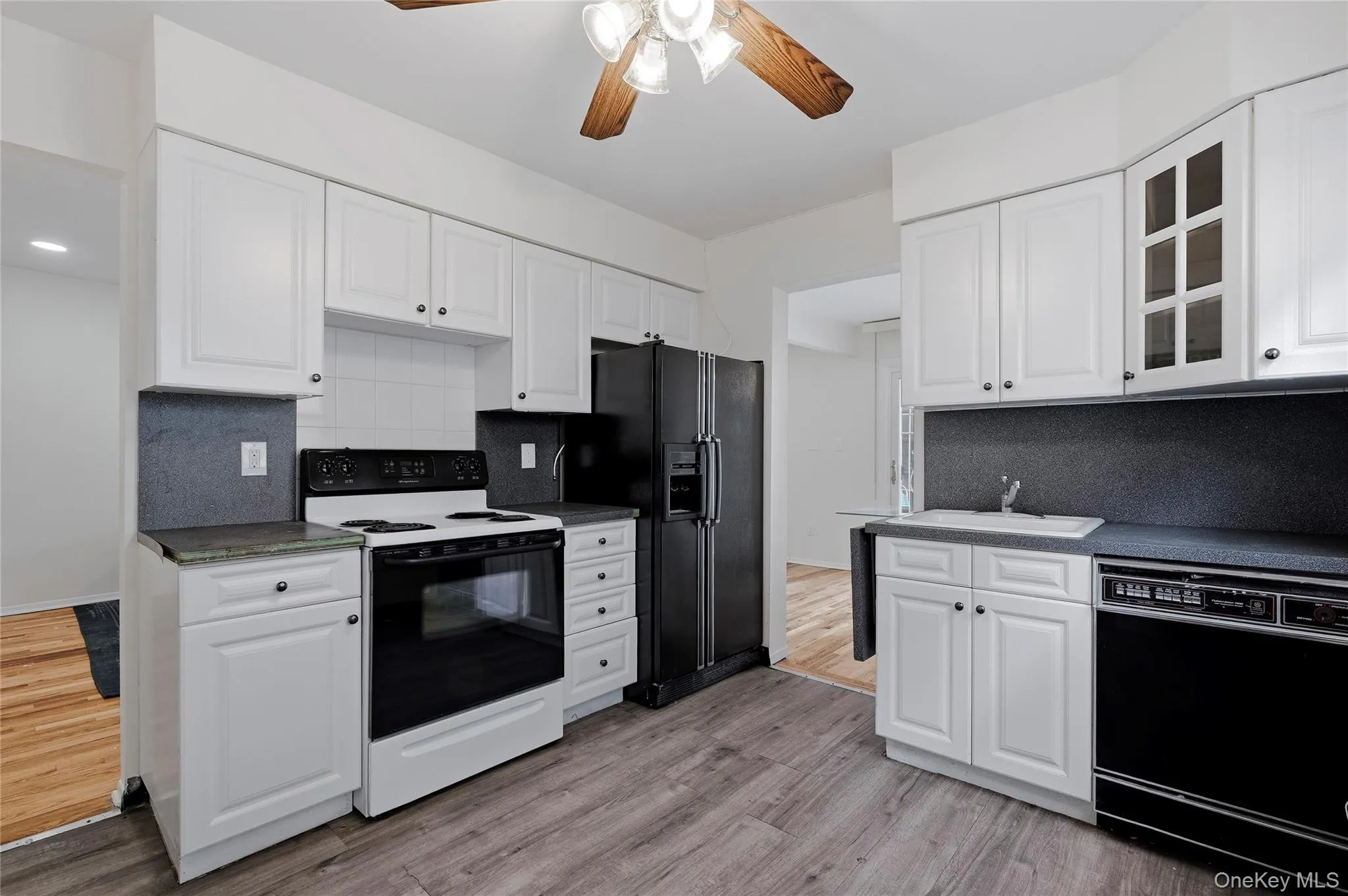 Kitchen with black appliances, white cabinets, decorative backsplash, and dark countertops Kitchen with black appliances, white cabinets, decorative backsplash, and dark countertops