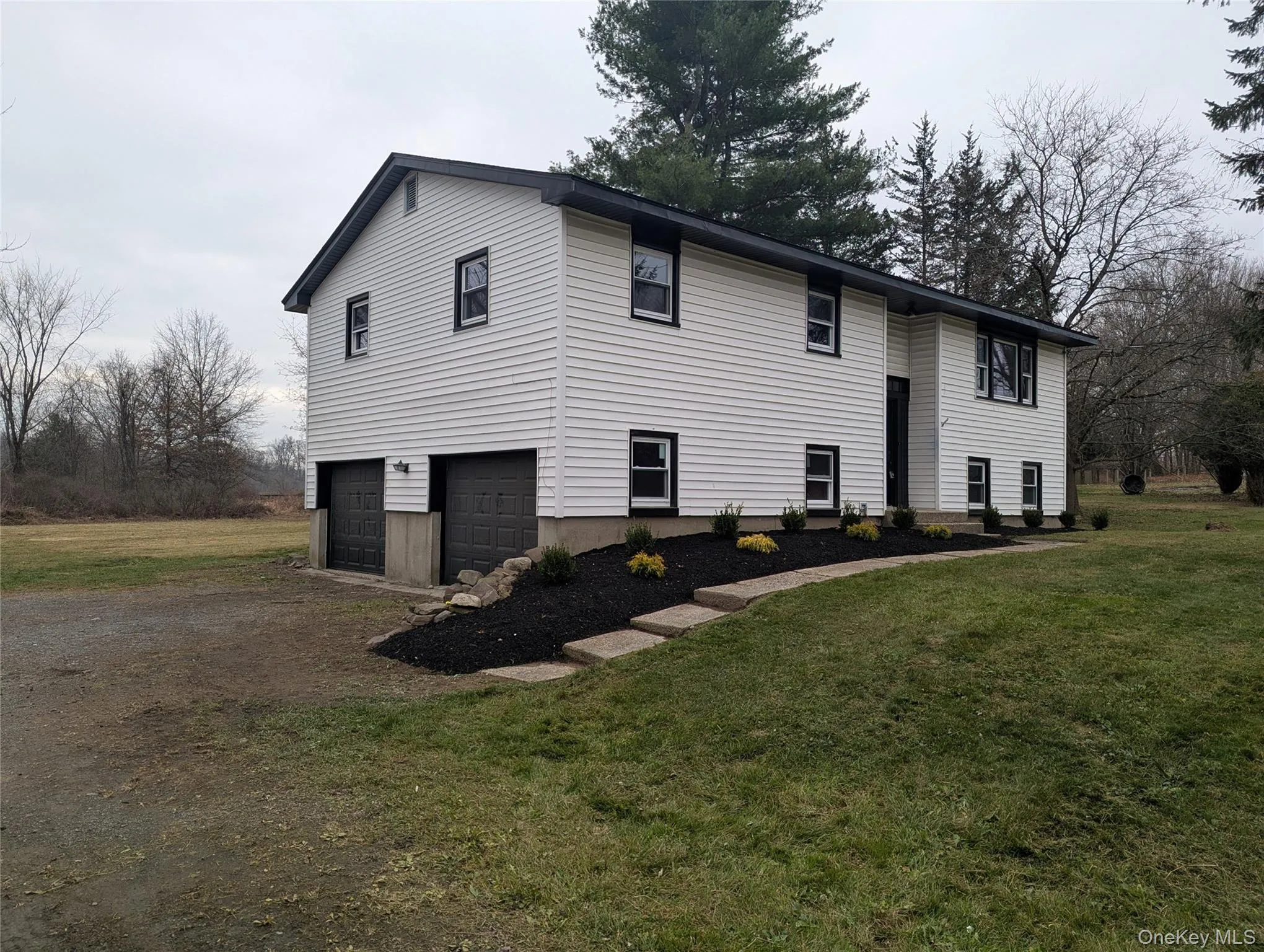View of front of home featuring a front lawn, dirt driveway, and an attached garage View of front of home featuring a front lawn, dirt driveway, and an attached garage