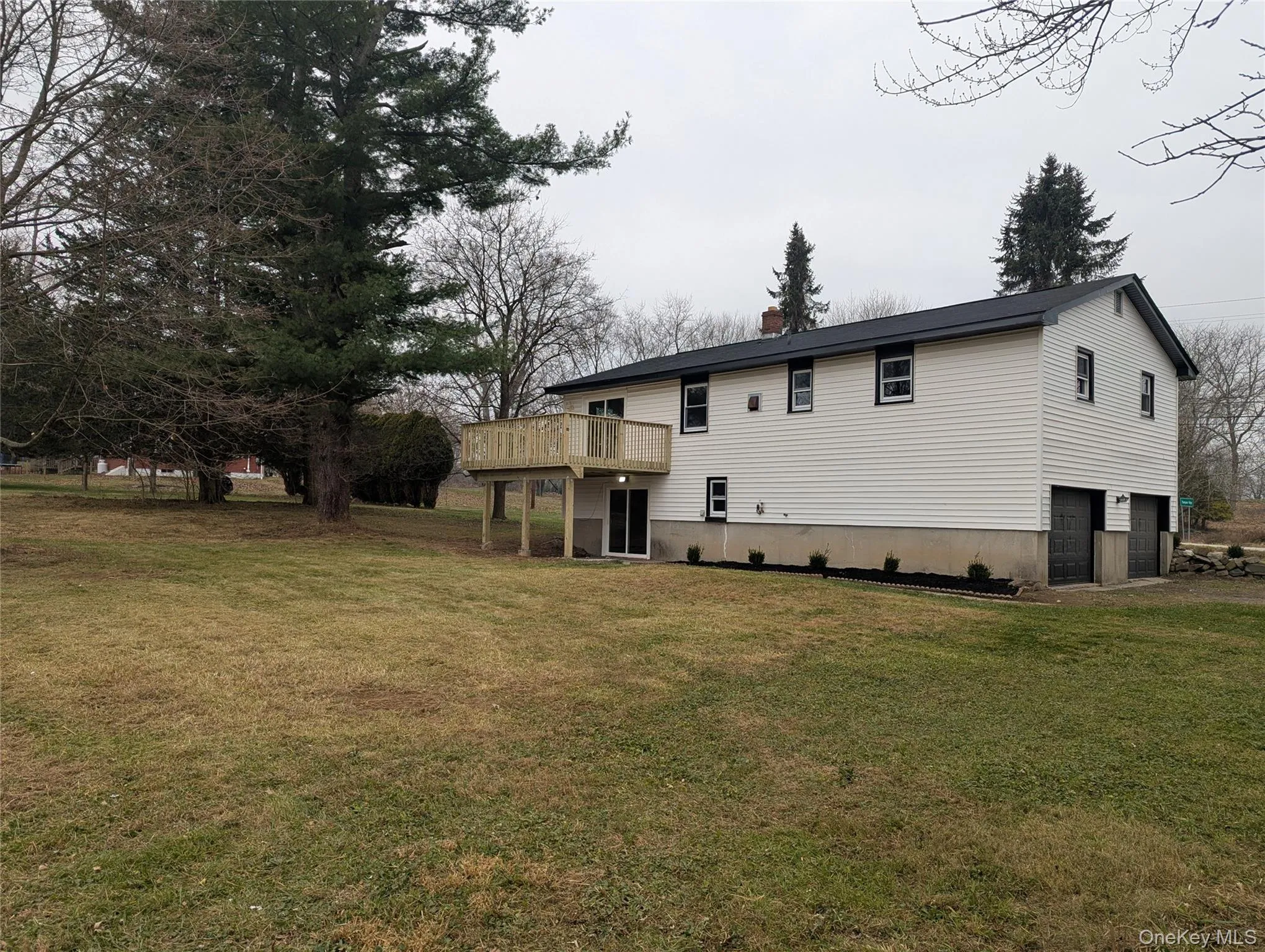 Rear view of property with a lawn, a garage, a chimney, and a deck Rear view of property with a lawn, a garage, a chimney, and a deck
