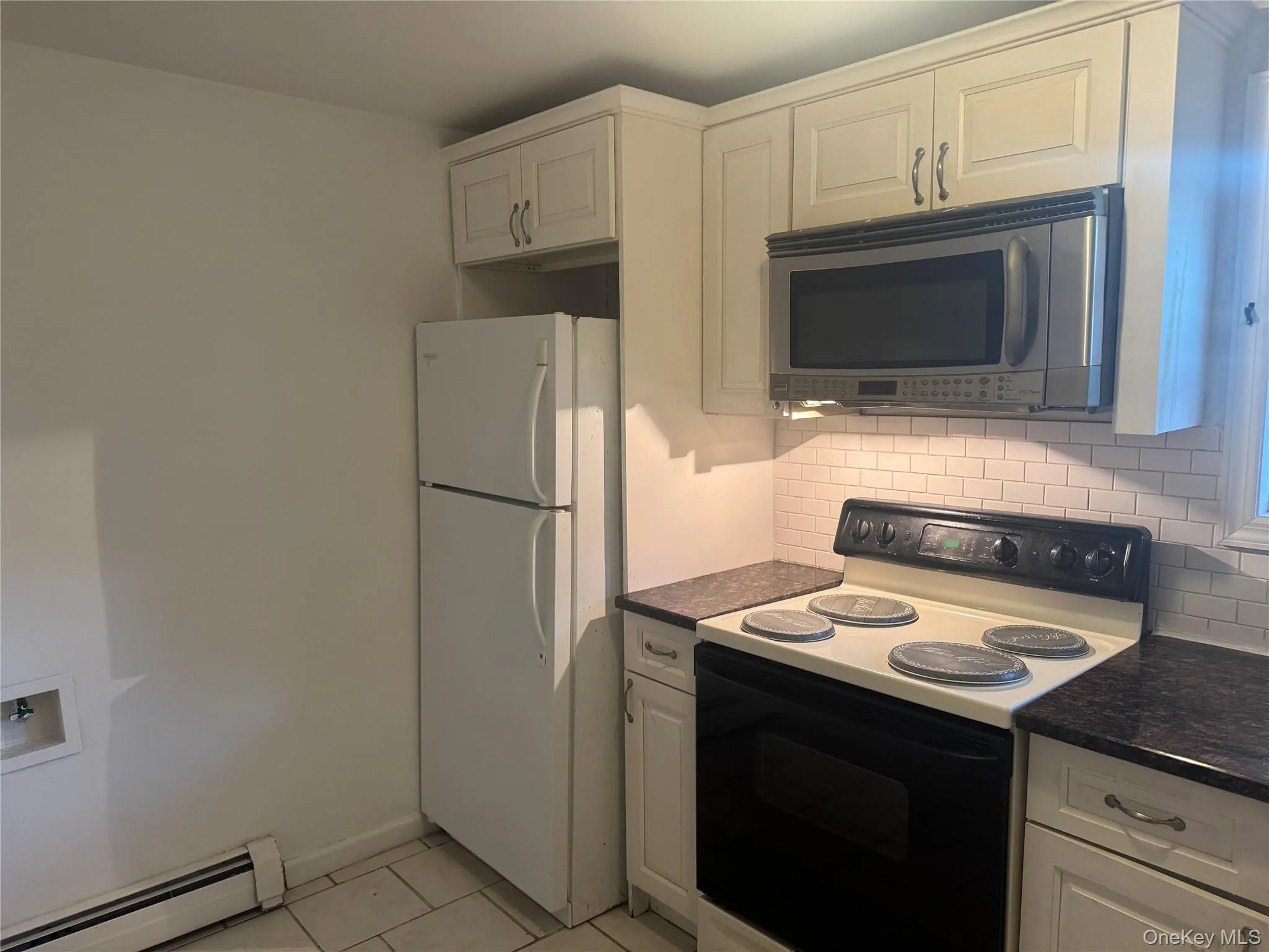 Kitchen featuring black / electric stove, stainless steel microwave, a baseboard heating unit, freestanding refrigerator, and light tile patterned floors Kitchen featuring black / electric stove, stainless steel microwave, a baseboard heating unit, freestanding refrigerator, and light tile patterned floors