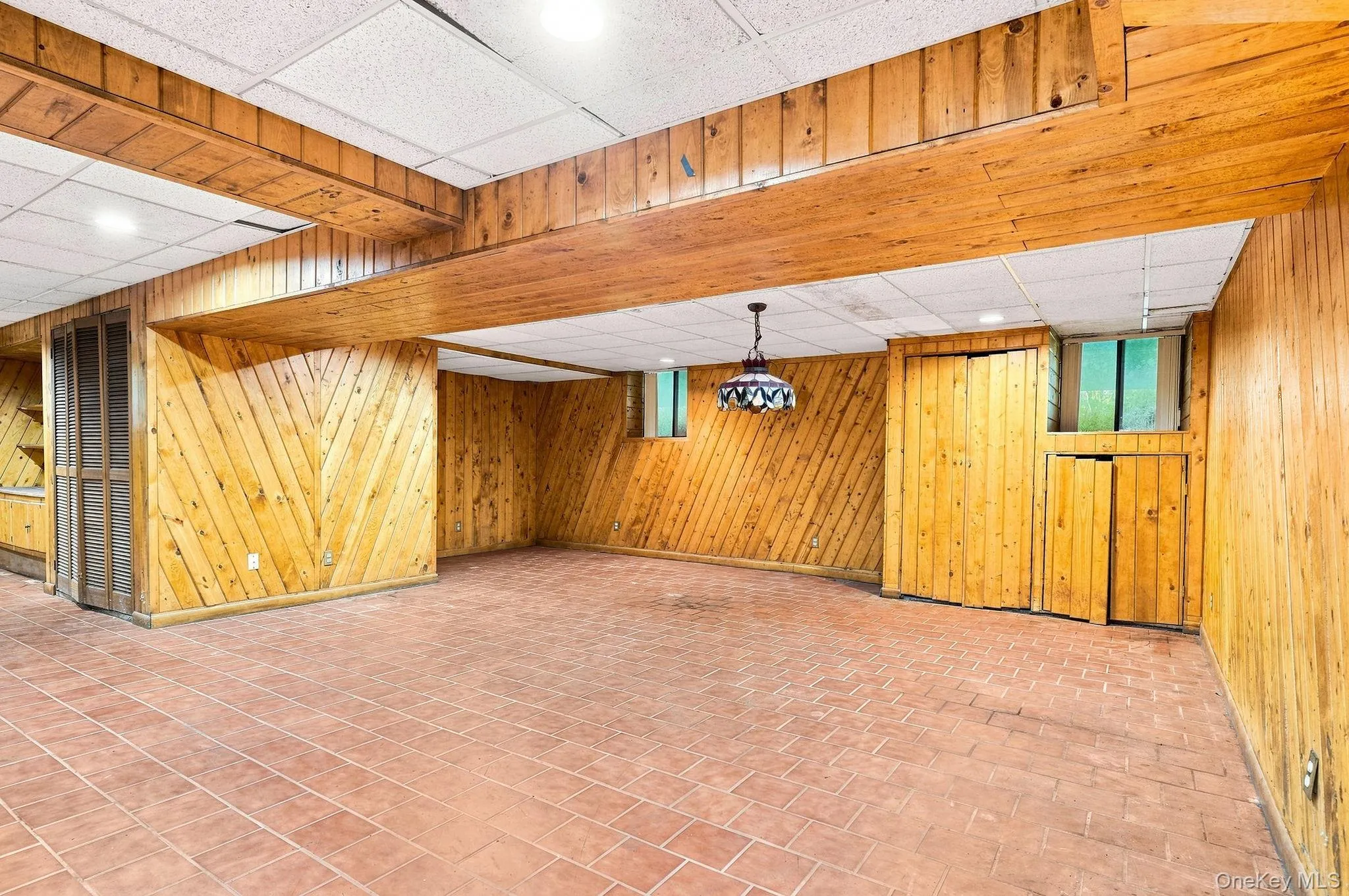 Spacious room featuring wood paneling, tiled flooring, wood beam accents, and integrated lighting Spacious room featuring wood paneling, tiled flooring, wood beam accents, and integrated lighting