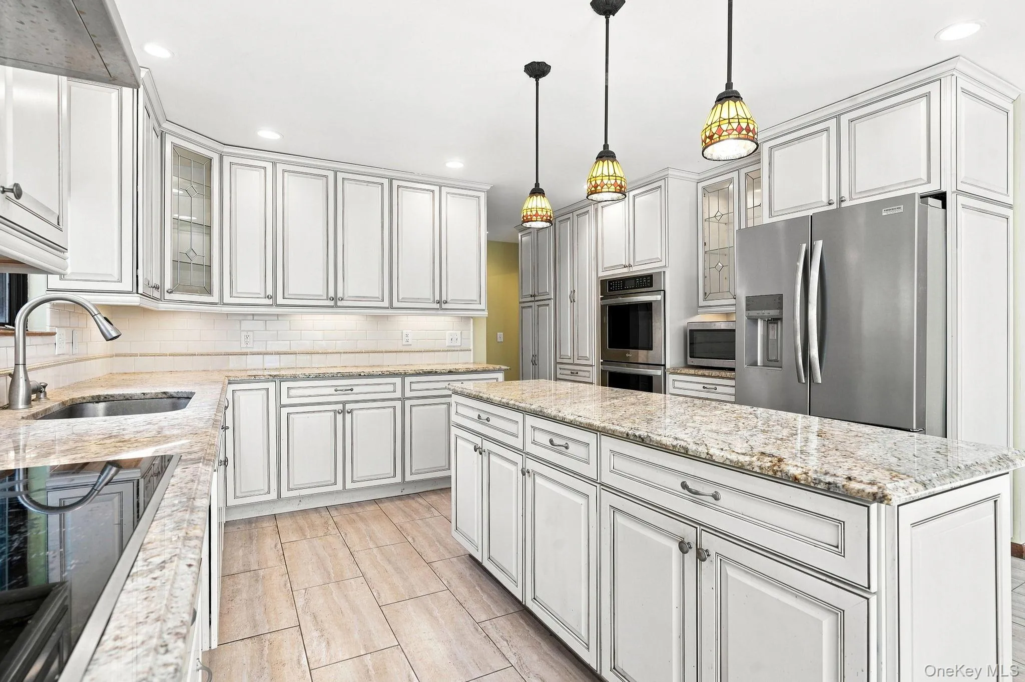 White cabinetry with dark contrasting trim, light-toned stone countertops, stainless steel appliances, tile flooring, and decorative pendant lighting White cabinetry with dark contrasting trim, light-toned stone countertops, stainless steel appliances, tile flooring, and decorative pendant lighting