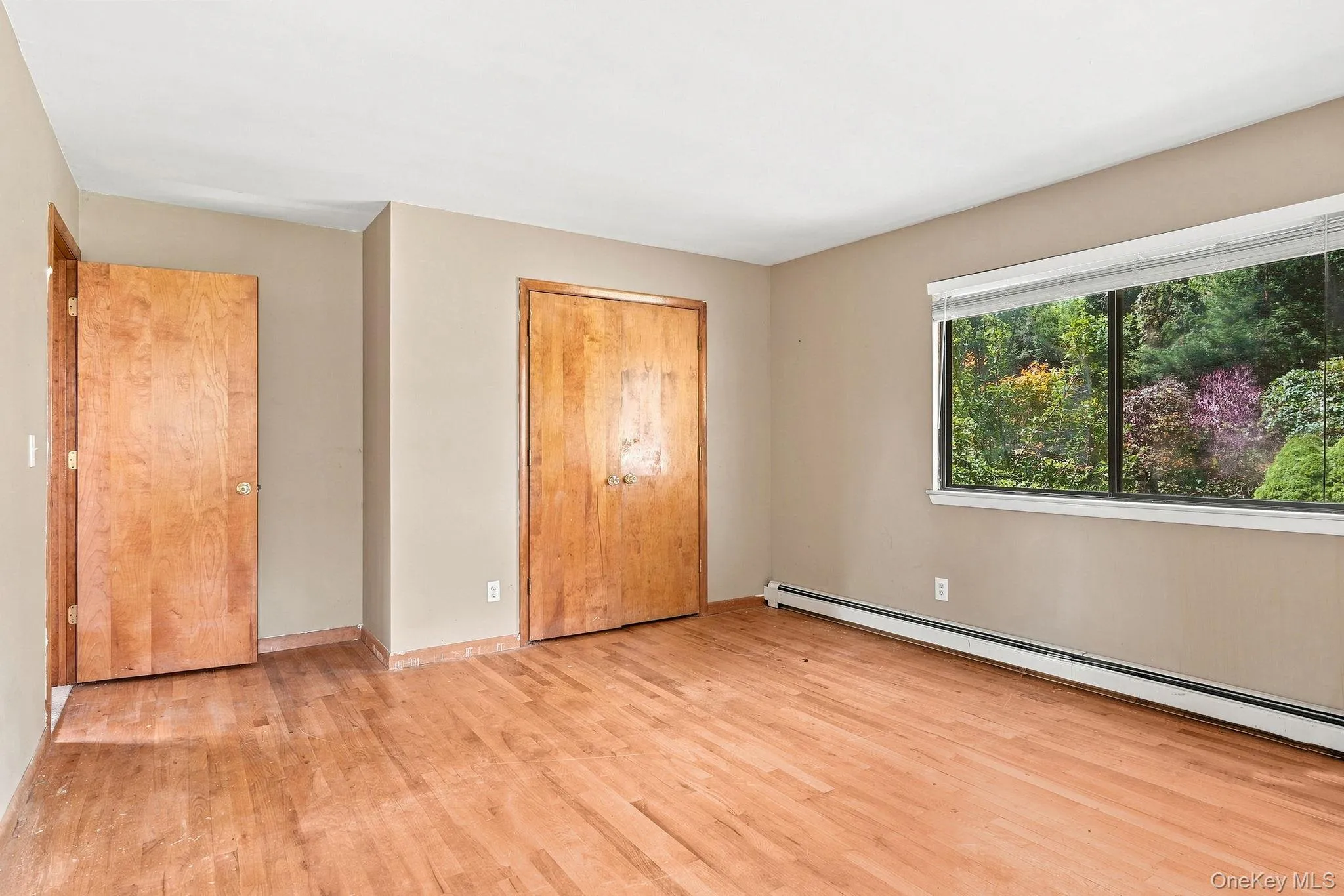 Wood-finish flooring, neutral wall tones, and a large window with natural scenery Wood-finish flooring, neutral wall tones, and a large window with natural scenery