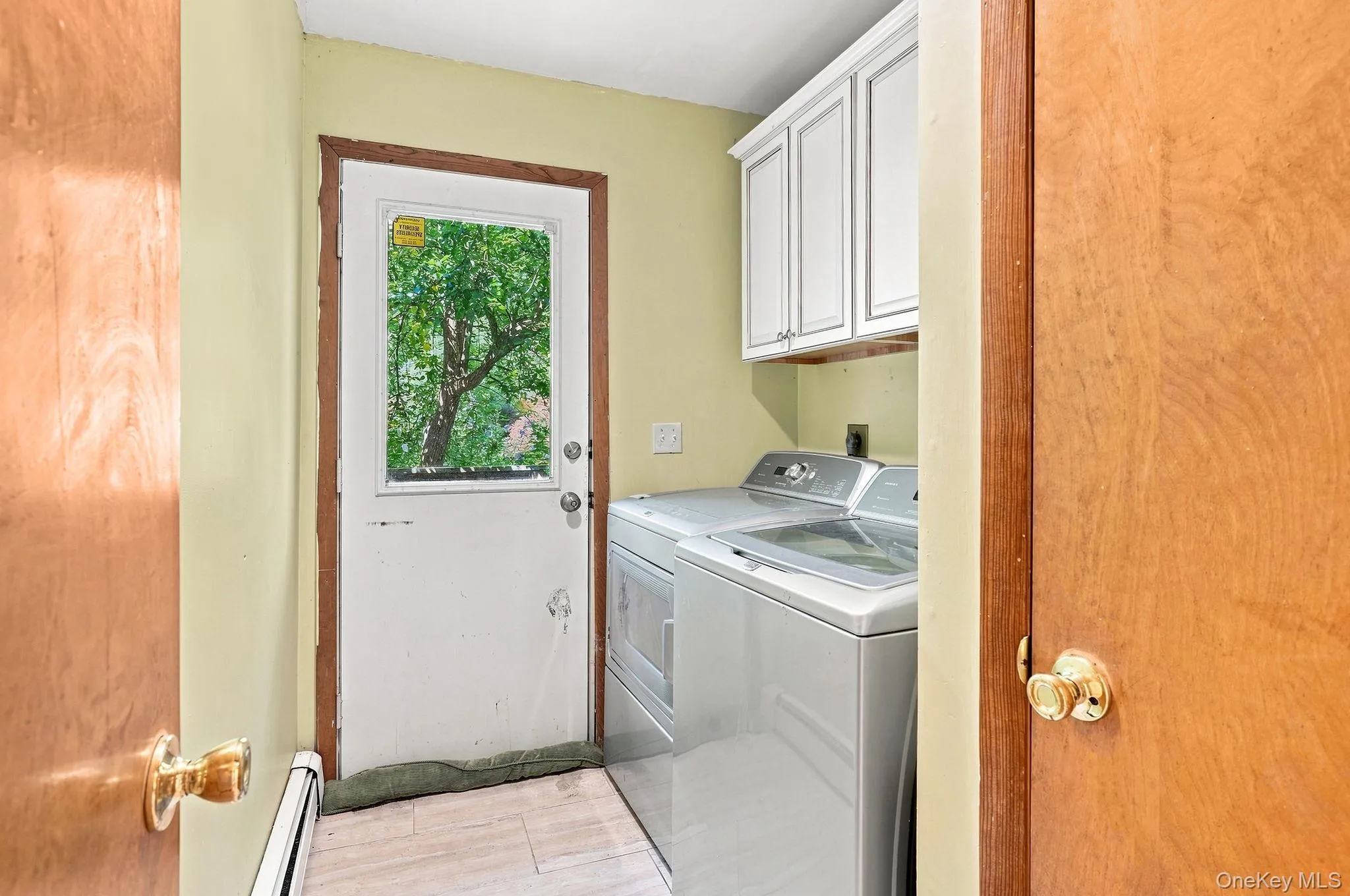 Utility area with white wall-mounted cabinetry, a white door with a window, and light-toned flooring Utility area with white wall-mounted cabinetry, a white door with a window, and light-toned flooring