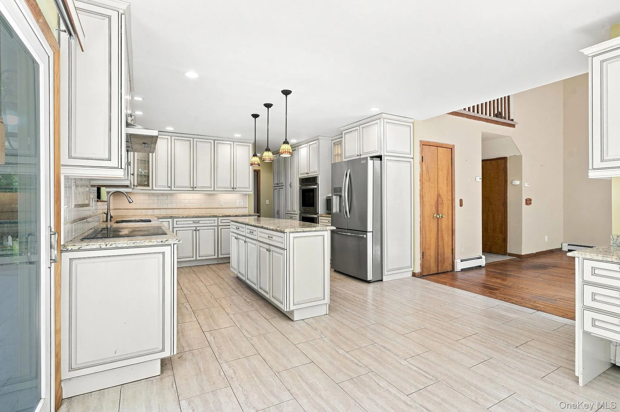 Spacious kitchen featuring white paneled cabinetry, stainless steel appliances, a center island with pendant lighting, and light-toned tile flooring Spacious kitchen featuring white paneled cabinetry, stainless steel appliances, a center island with pendant lighting, and light-toned tile flooring