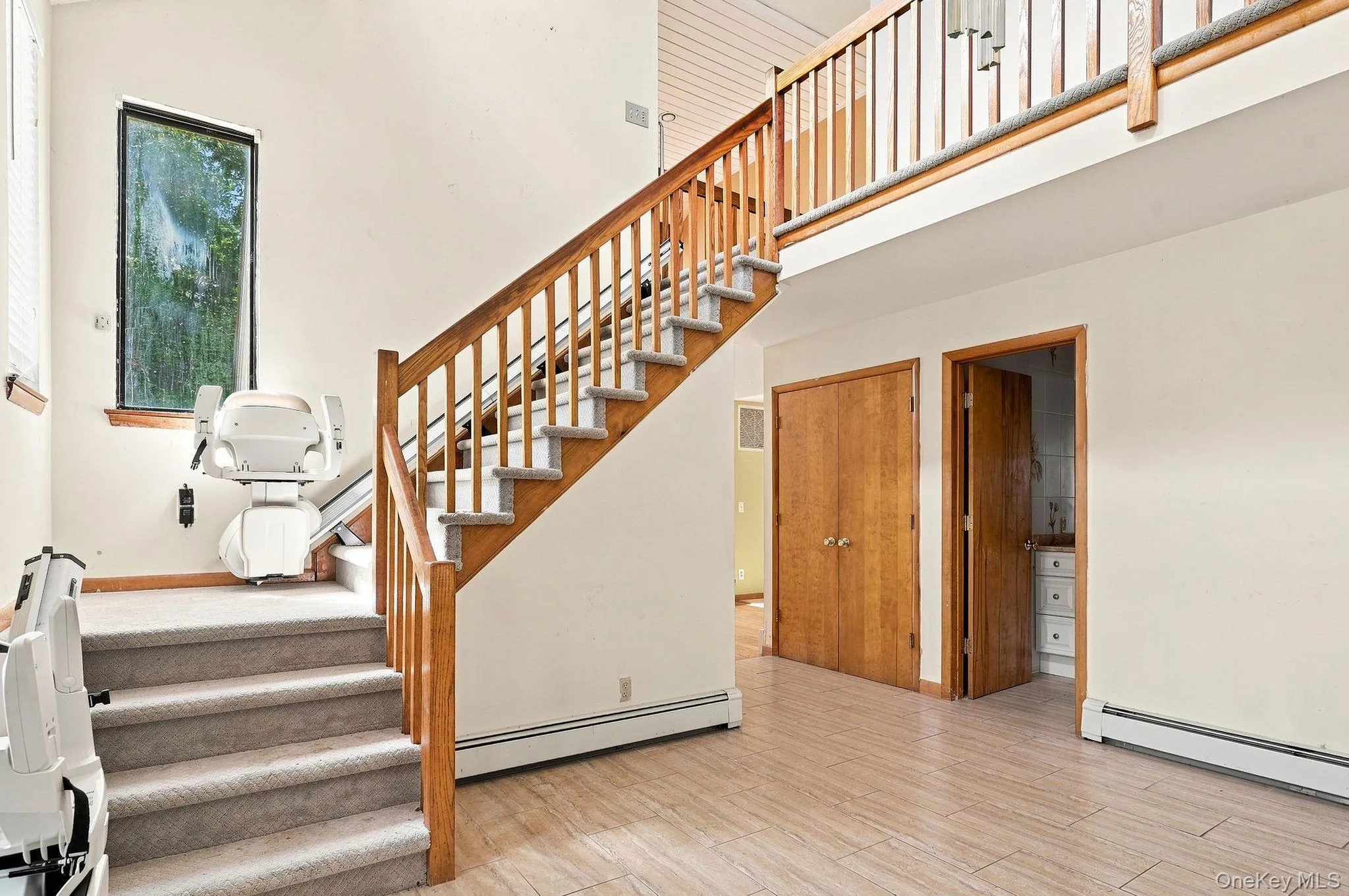 Open-concept interior featuring light-toned flooring and a wooden staircase with carpeted treads Open-concept interior featuring light-toned flooring and a wooden staircase with carpeted treads