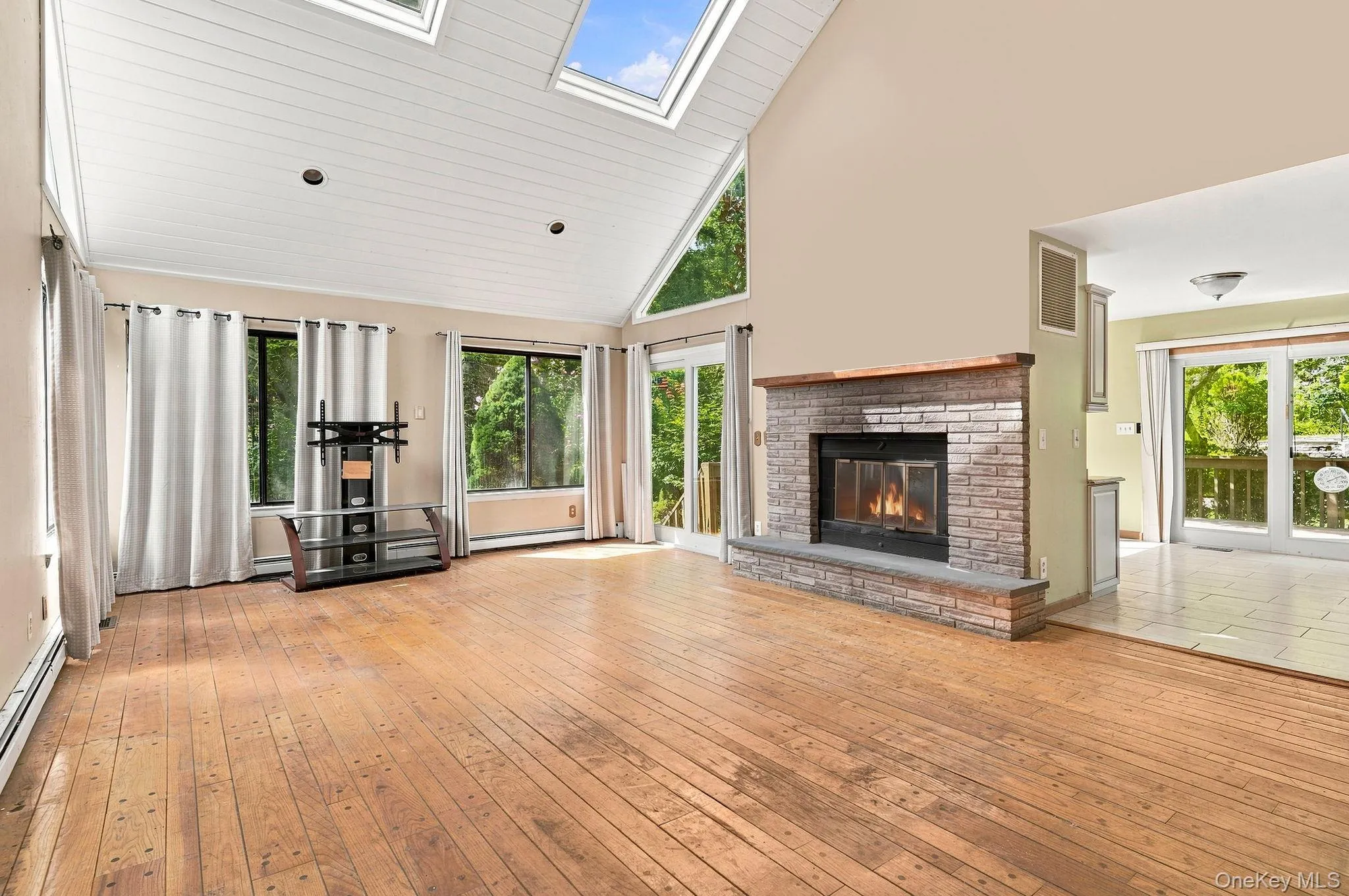 Vaulted ceiling with skylights, wood-finish flooring, stone-faced fireplace, and sliding glass doors Vaulted ceiling with skylights, wood-finish flooring, stone-faced fireplace, and sliding glass doors