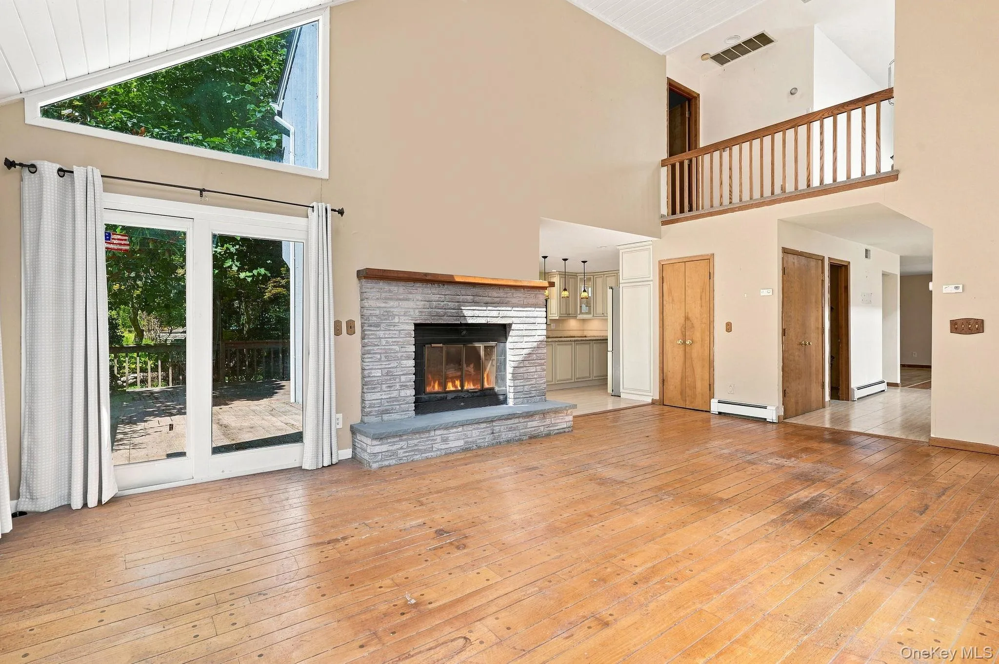 Hardwood flooring, stone fireplace with hearth, vaulted ceiling, upper-level landing with wood railing, and glass patio doors Hardwood flooring, stone fireplace with hearth, vaulted ceiling, upper-level landing with wood railing, and glass patio doors