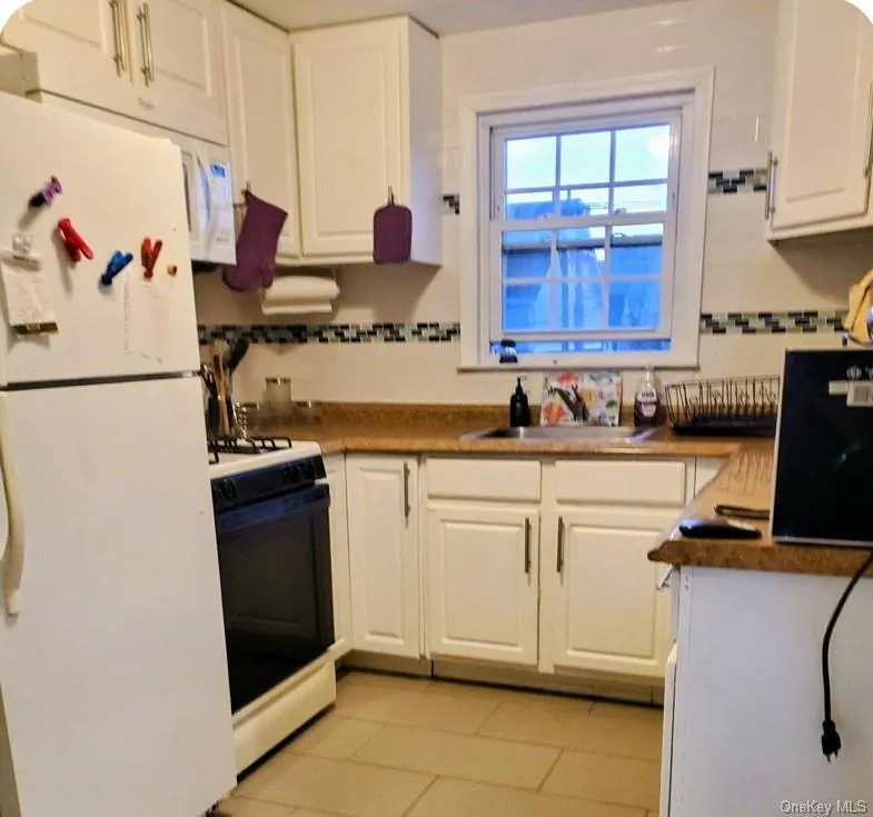 Kitchen featuring white appliances, white cabinets, light tile patterned floors, and tasteful backsplash Kitchen featuring white appliances, white cabinets, light tile patterned floors, and tasteful backsplash