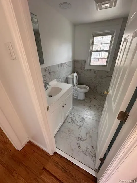 Half bath featuring vanity, tile walls, and a wainscoted wall Half bath featuring vanity, tile walls, and a wainscoted wall