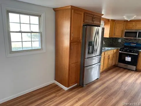 Kitchen featuring brown cabinets, stainless steel appliances, decorative backsplash, and dark wood finished floors Kitchen featuring brown cabinets, stainless steel appliances, decorative backsplash, and dark wood finished floors