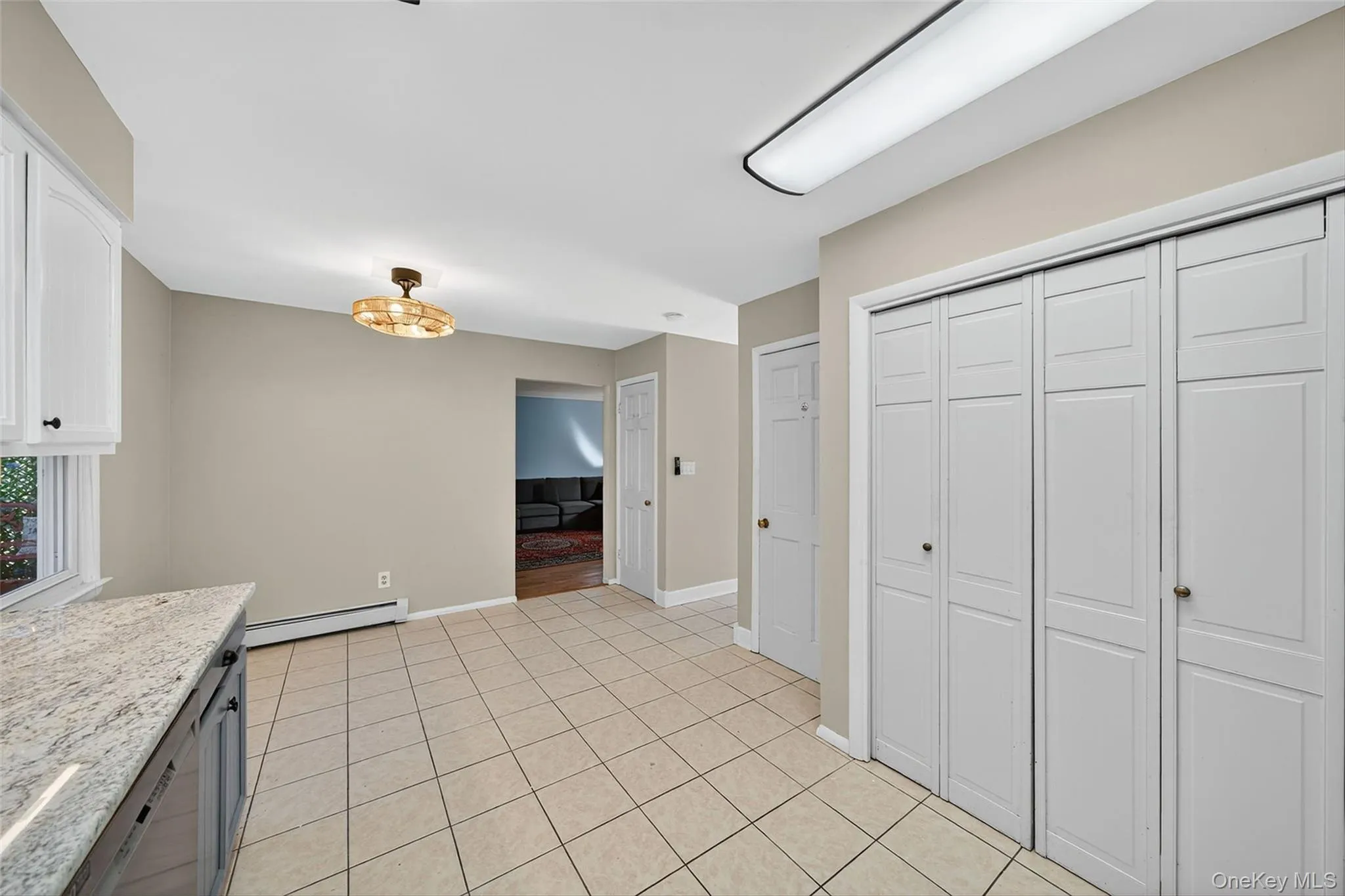 Kitchen featuring baseboard heating, light tile patterned floors, light stone countertops, and white cabinetry Kitchen featuring baseboard heating, light tile patterned floors, light stone countertops, and white cabinetry