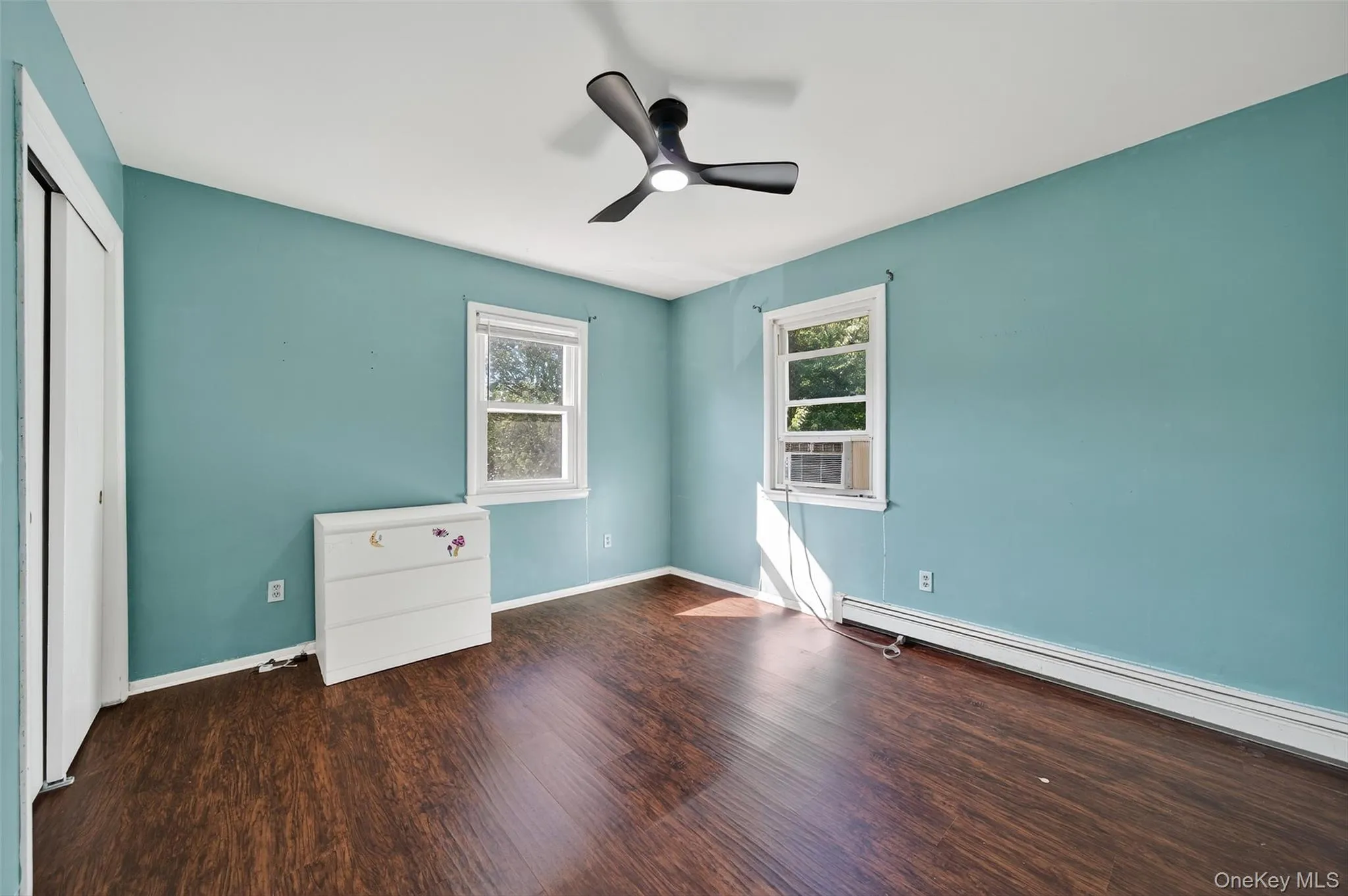 Unfurnished bedroom with dark wood finished floors, ceiling fan, a closet, and a baseboard radiator Unfurnished bedroom with dark wood finished floors, ceiling fan, a closet, and a baseboard radiator