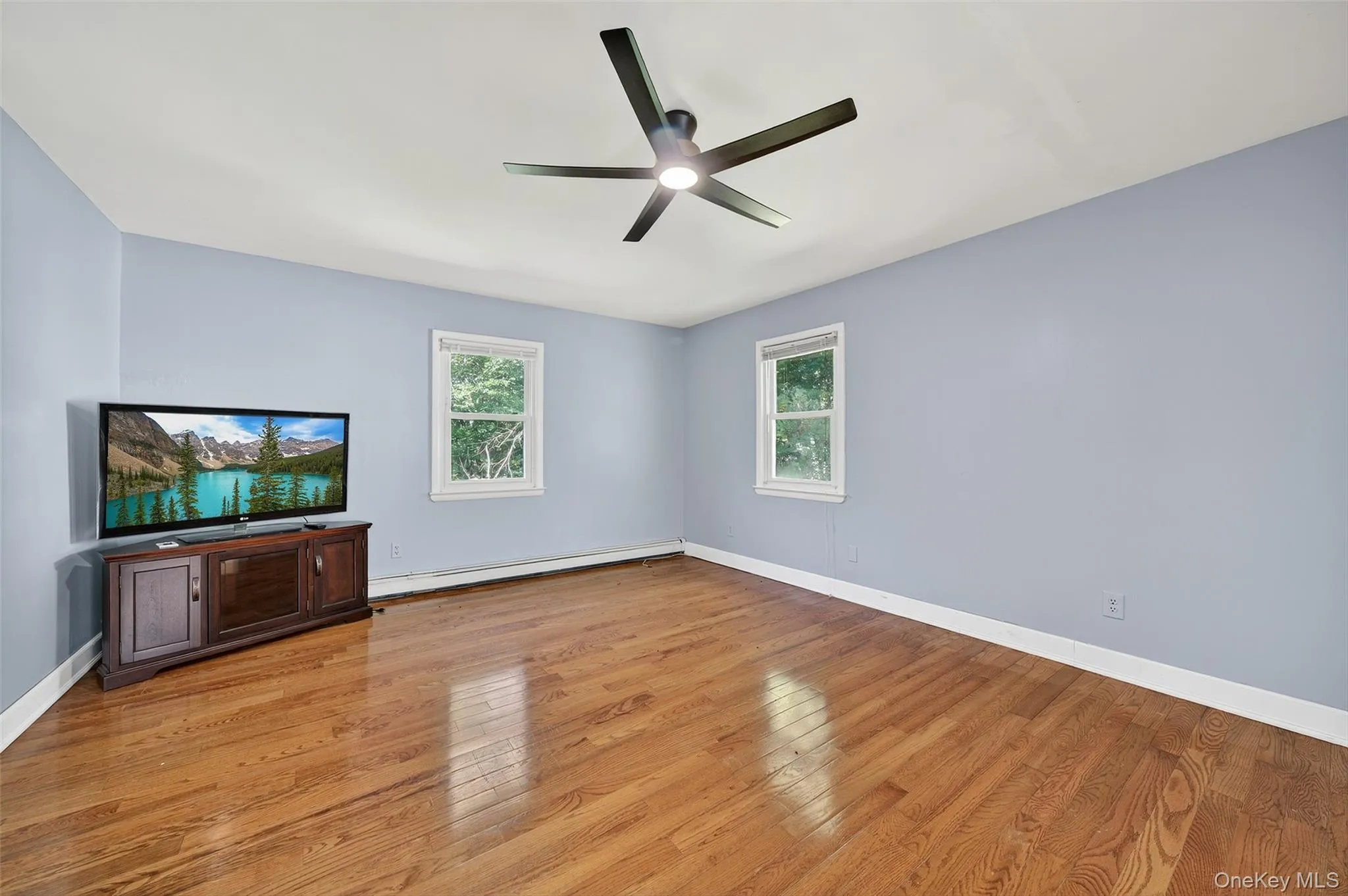 Unfurnished living room featuring light wood-type flooring, a baseboard heating unit, and ceiling fan Unfurnished living room featuring light wood-type flooring, a baseboard heating unit, and ceiling fan