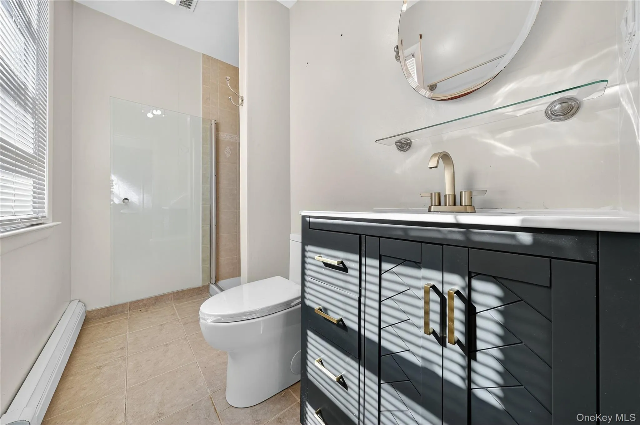 Full bath with a baseboard heating unit, vanity, light tile patterned floors, and a stall shower Full bath with a baseboard heating unit, vanity, light tile patterned floors, and a stall shower