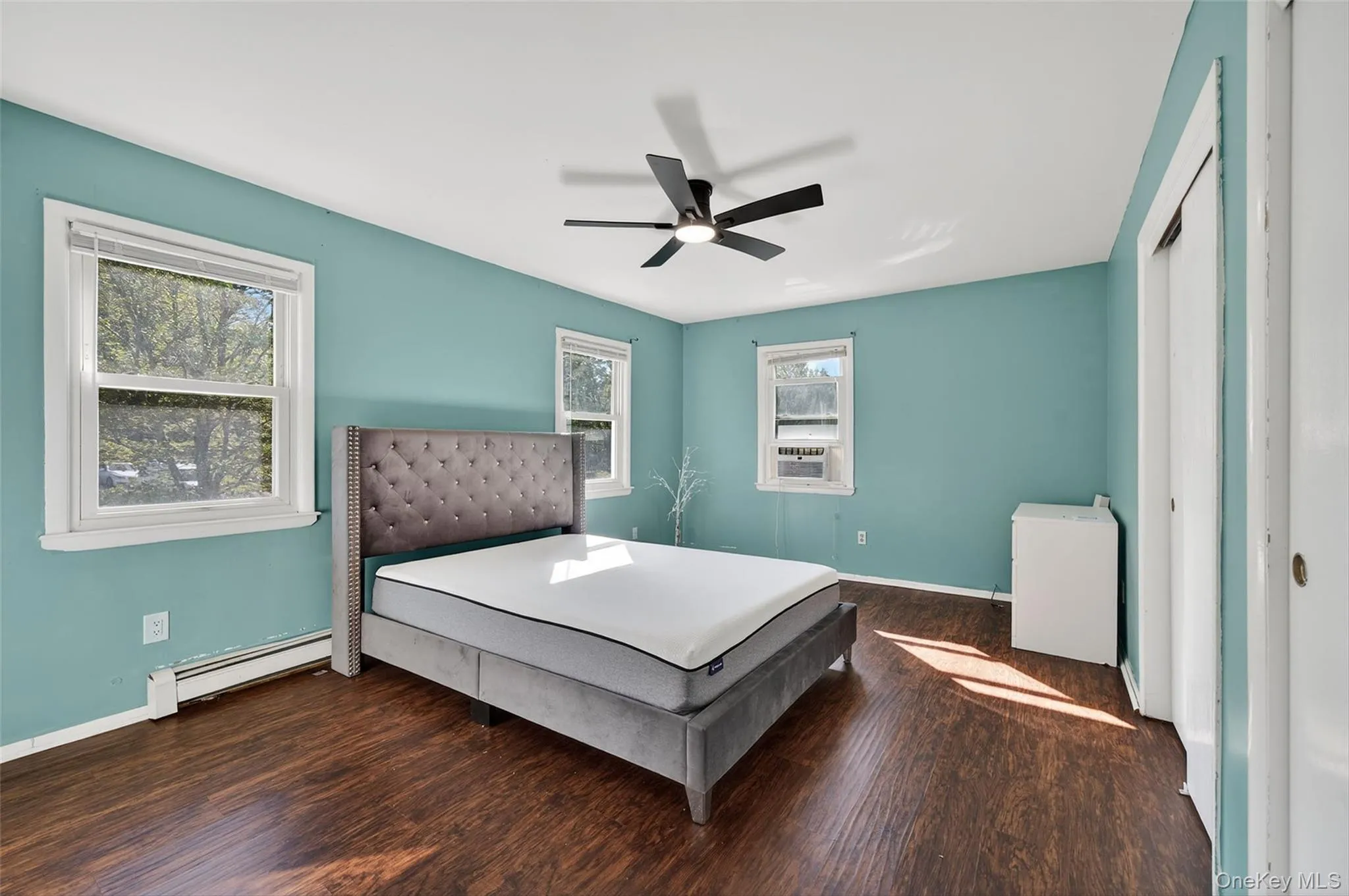 Bedroom featuring dark wood-style floors, multiple windows, baseboard heating, and ceiling fan Bedroom featuring dark wood-style floors, multiple windows, baseboard heating, and ceiling fan
