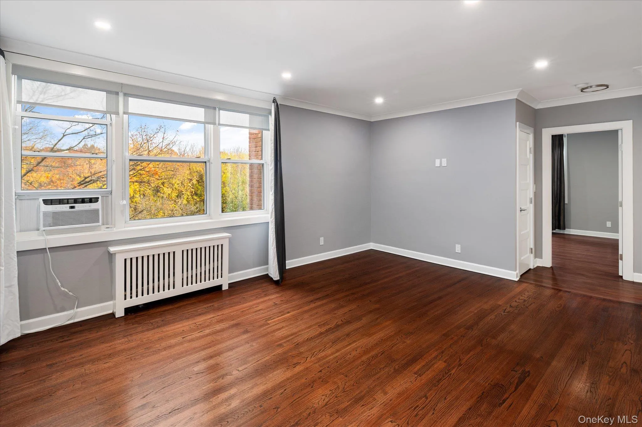 Empty room featuring radiator, recessed lighting, crown molding, dark wood-style flooring, and cooling unit Empty room featuring radiator, recessed lighting, crown molding, dark wood-style flooring, and cooling unit