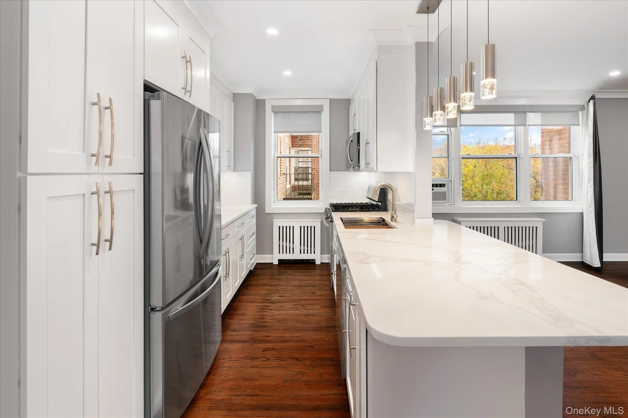 Kitchen with dark wood finished floors, stainless steel appliances, light stone countertops, white cabinetry, and hanging light fixtures Kitchen with dark wood finished floors, stainless steel appliances, light stone countertops, white cabinetry, and hanging light fixtures