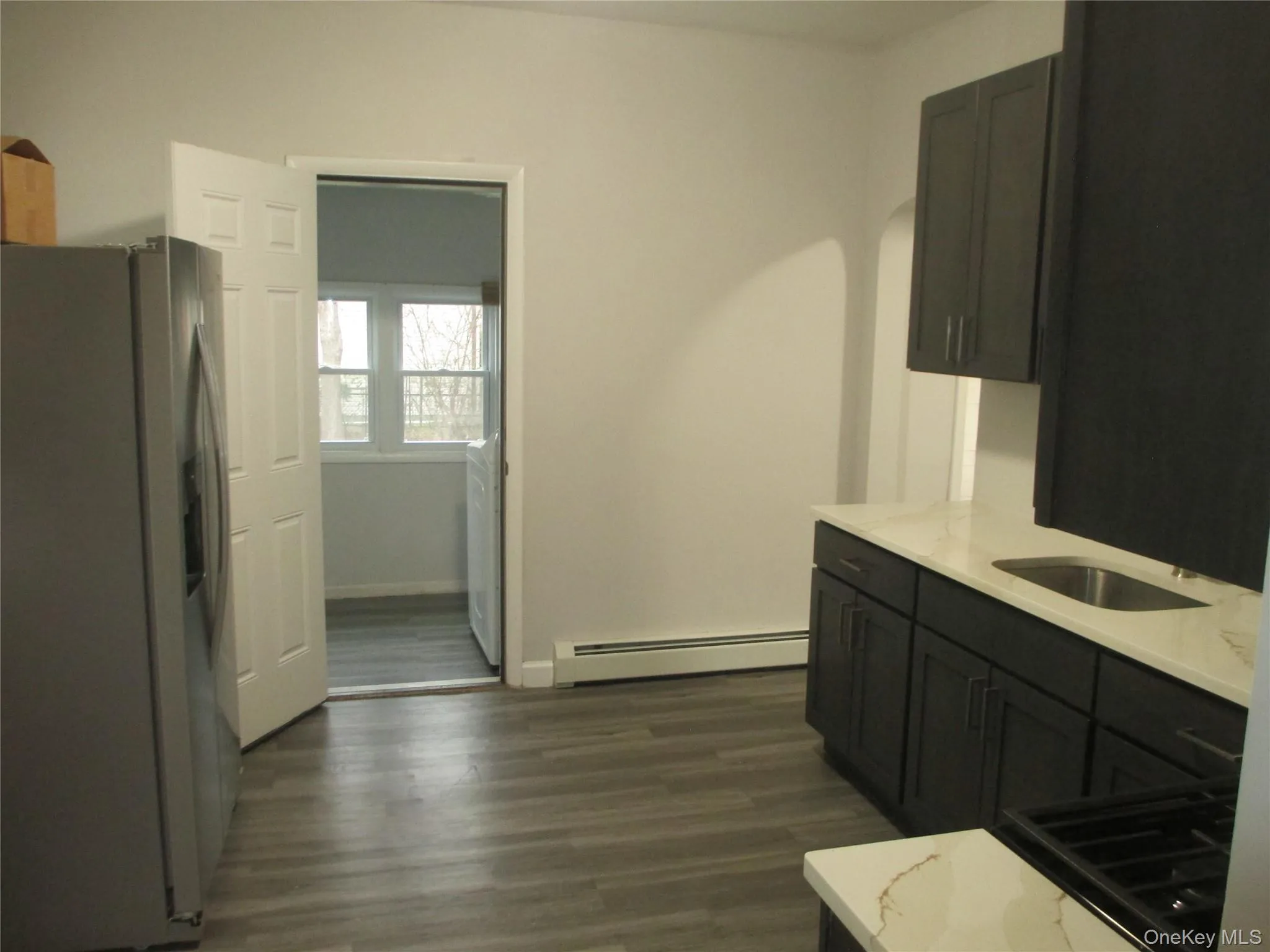 Kitchen featuring stainless steel fridge with ice dispenser, light stone countertops, dark wood-style floors, and a baseboard heating unit Kitchen featuring stainless steel fridge with ice dispenser, light stone countertops, dark wood-style floors, and a baseboard heating unit