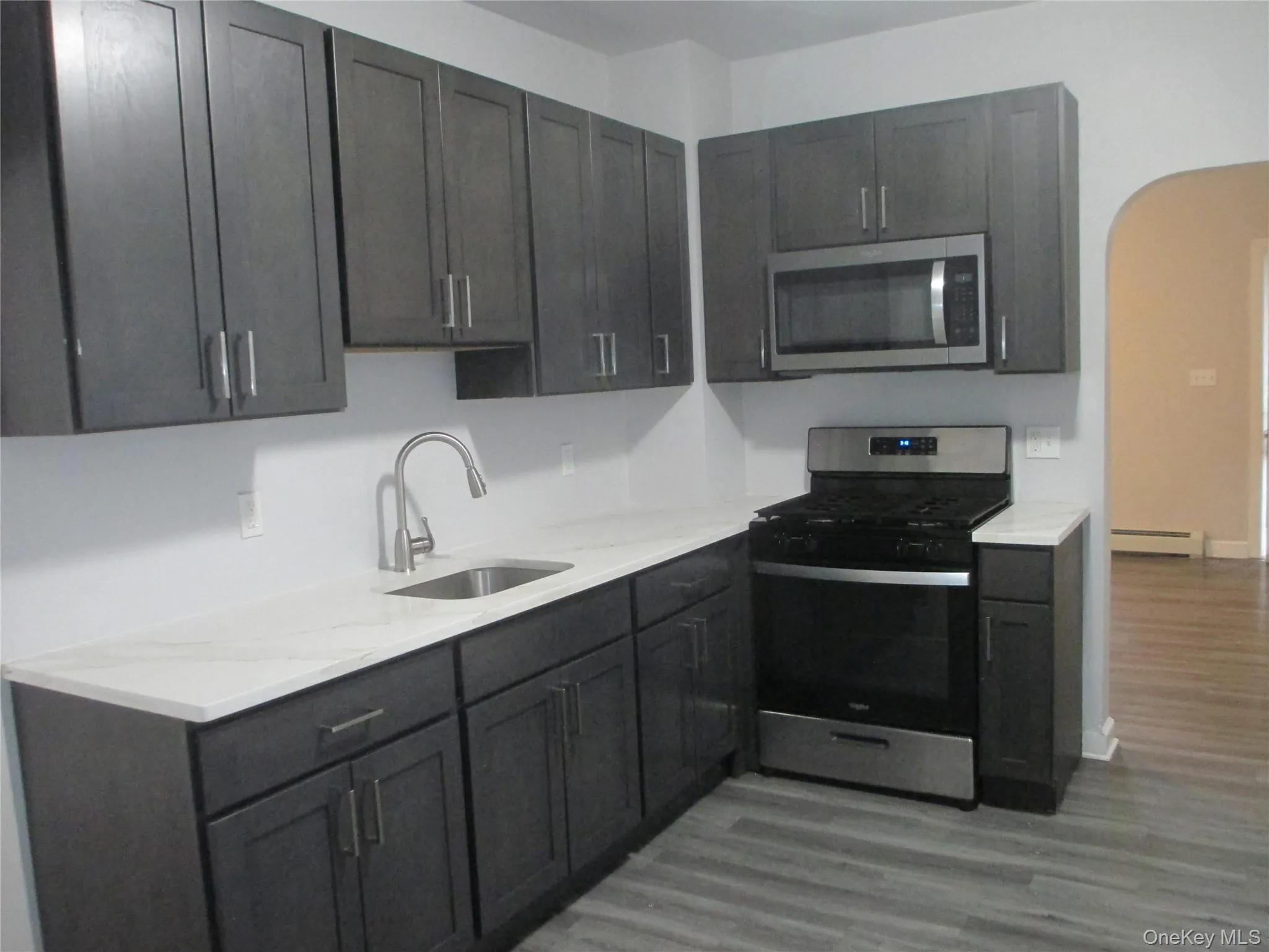 Kitchen with stainless steel appliances, arched walkways, dark wood finished floors, a baseboard heating unit, and light stone counters Kitchen with stainless steel appliances, arched walkways, dark wood finished floors, a baseboard heating unit, and light stone counters